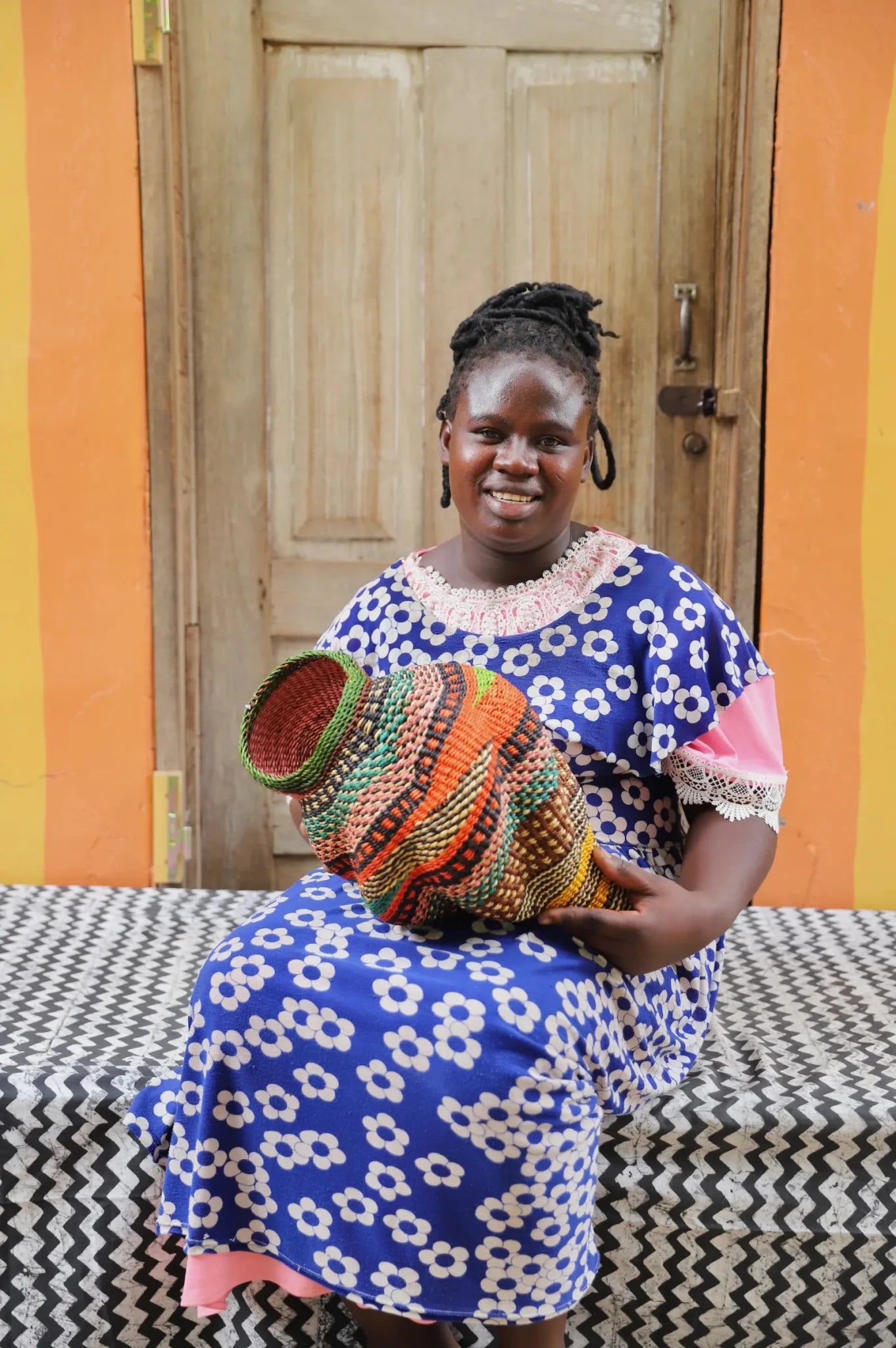Woman holding a woven conch piece on a black and white patterned surface with a wooden door in the background.