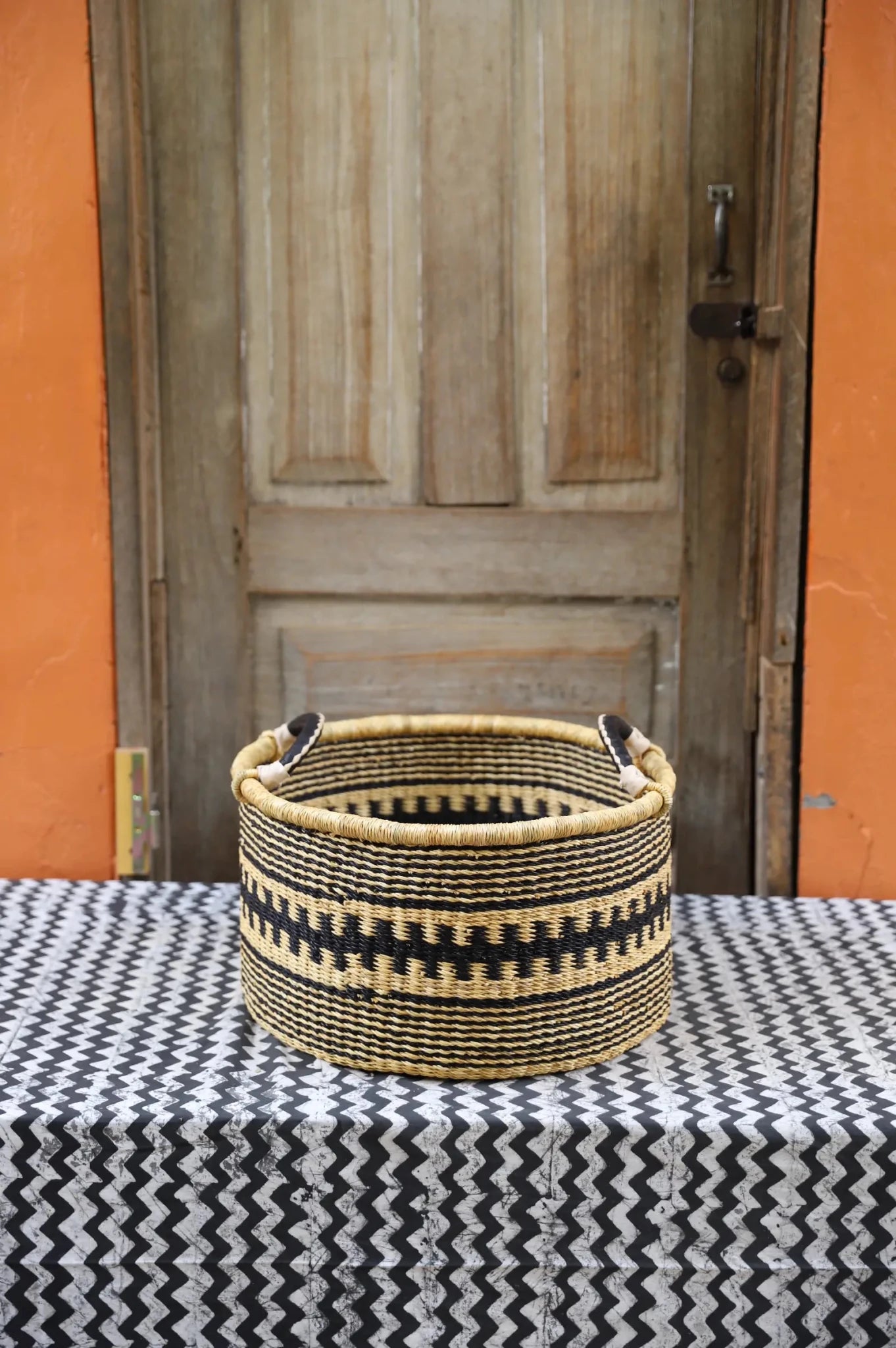 Woven Tub (Small) handwoven in Ghana sitting on black and white cloth with wooden door background
