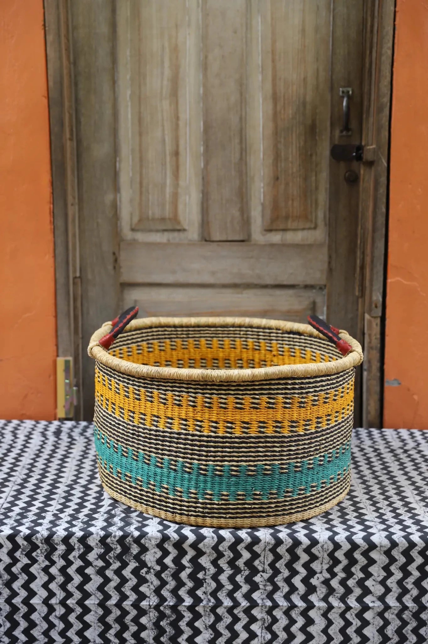 Woven Tub (Large) handwoven in Ghana sitting on black and white cloth with wooden door background
