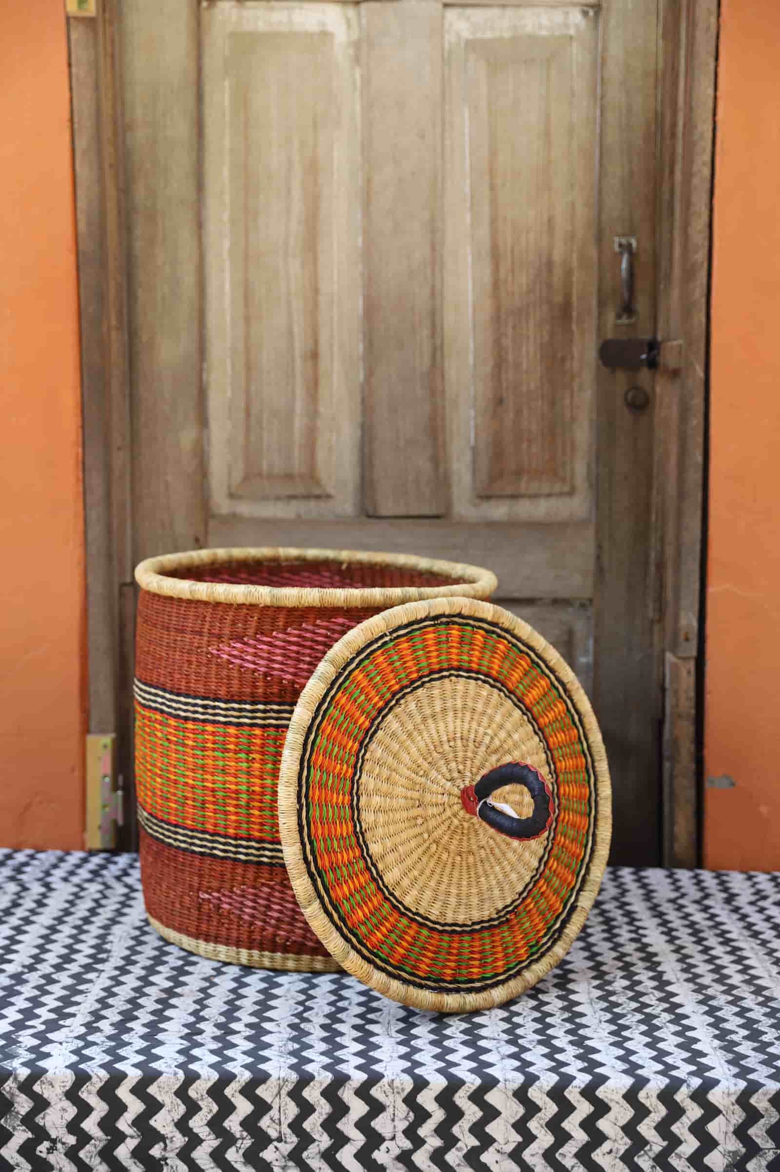 Woven basket with a lid on a table in front of a wooden door.