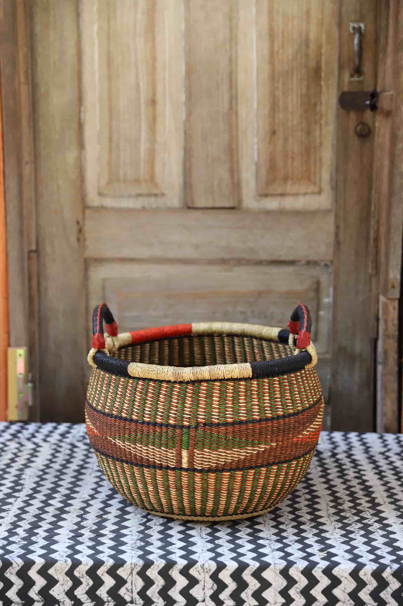 A colorful handwoven storage basket sitting on a black and white cloth against a wooden door