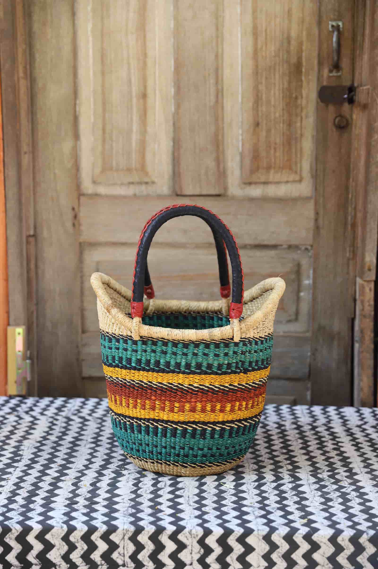 Woven carry on bag with premium leather handles on a black and white cloth against a wooden door.