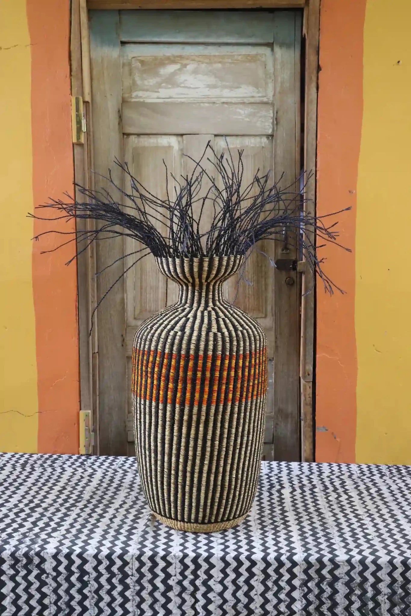 Decorative woven piece with stylish branches on a black and white cloth against a wooden door