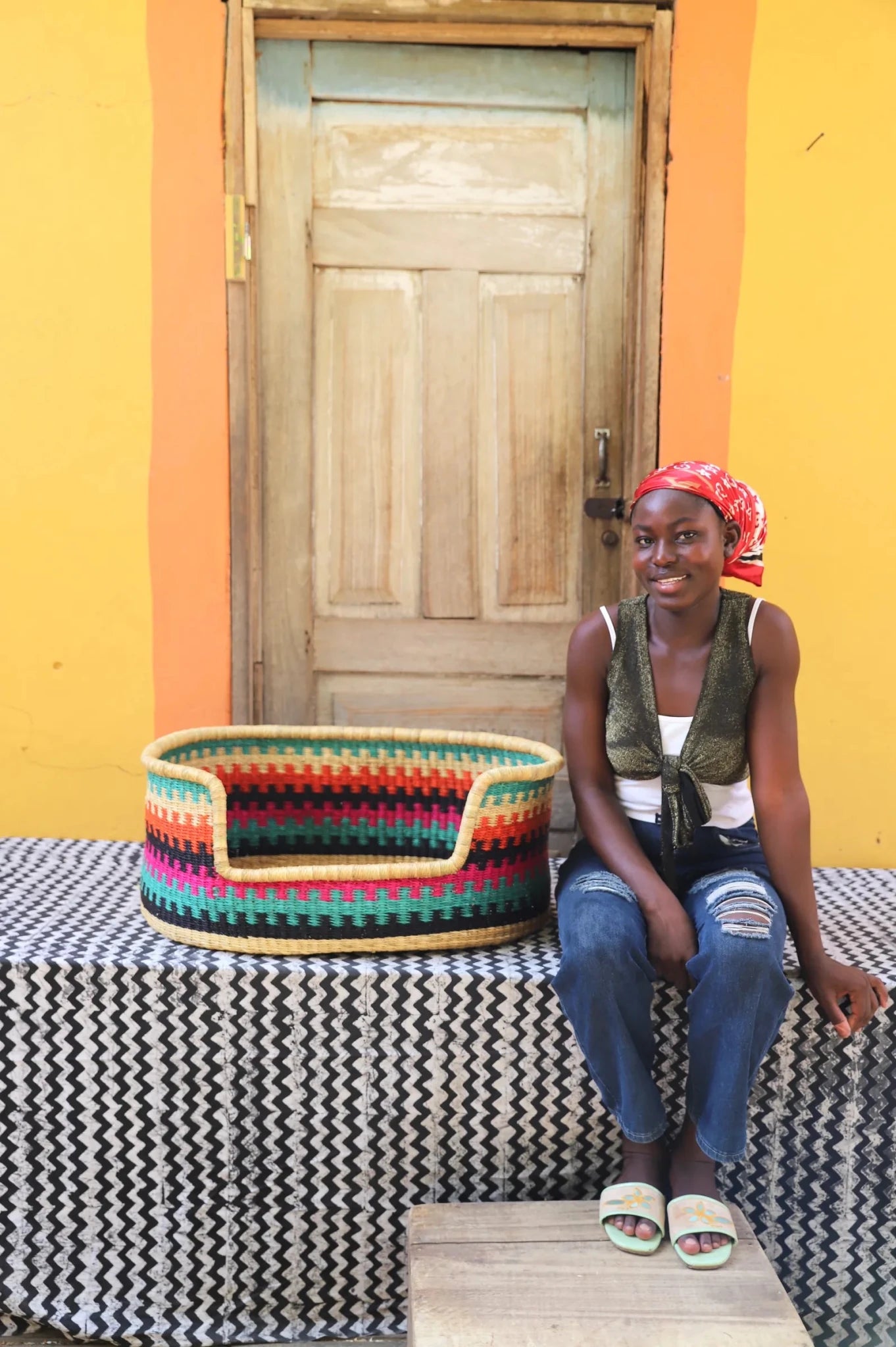 Woman  sitting on a bench with a woven basket next to a wooden door and yellow wall.
