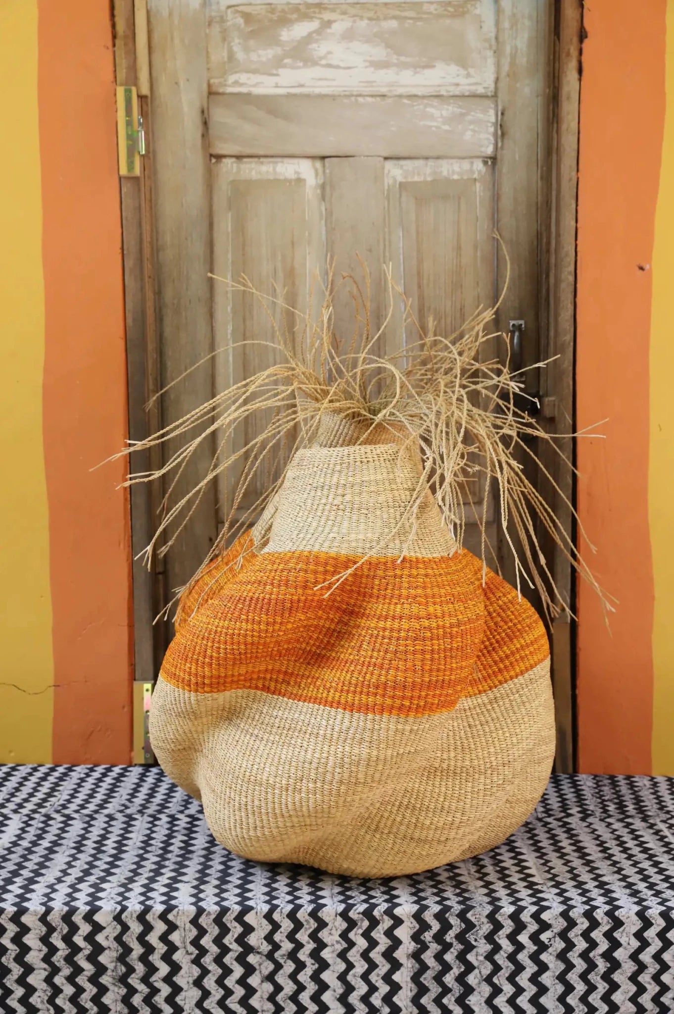Decorative basket with stylish straw branching out on a black and white cloth against a wooden door.