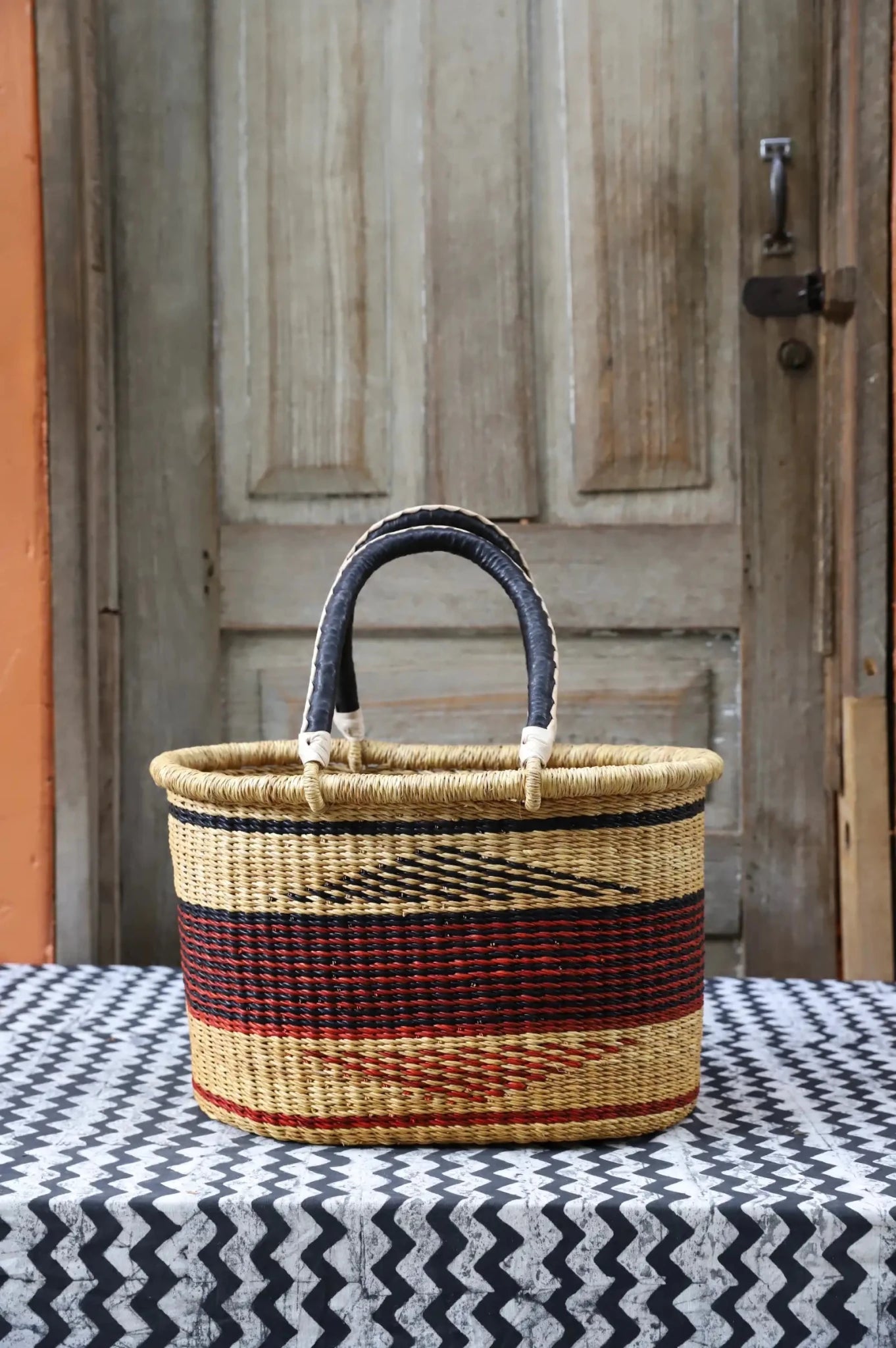 Woven carry on basket with premium leather on a black and white cloth against a wooden door