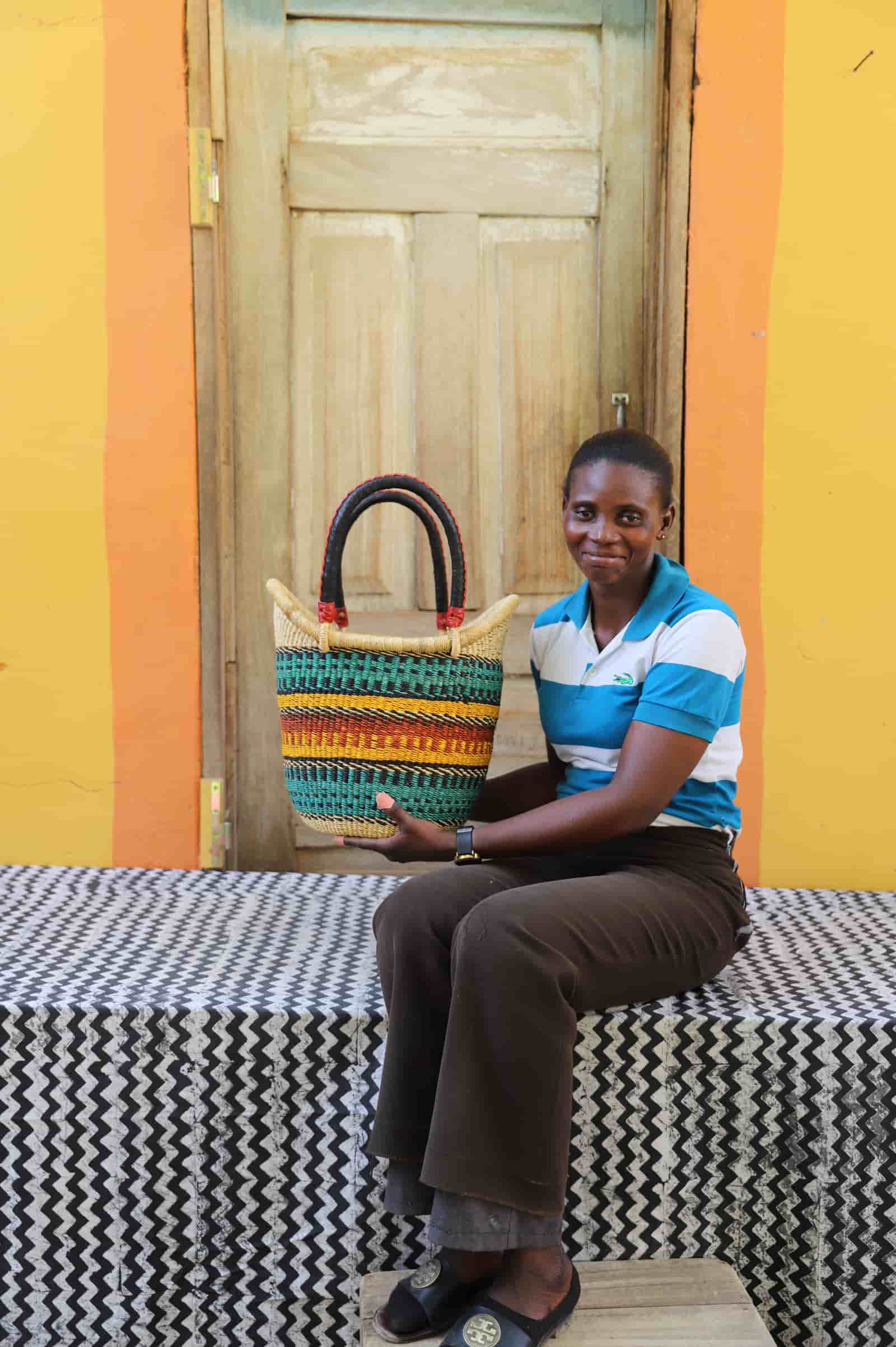 Artisan holding a colorful woven carry on bag with premium leather handles on a black and white cloth against a wooden door.