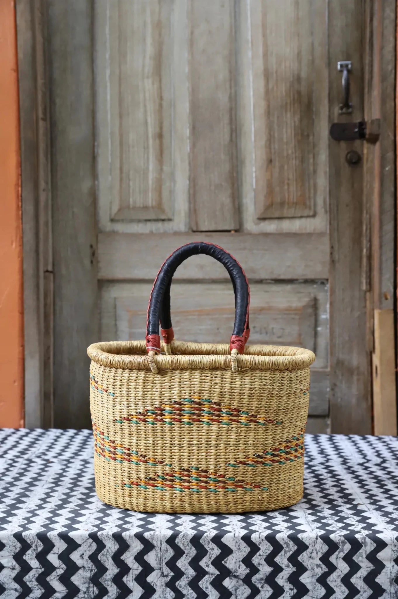 Woven carry on basket with premium leather on a black and white cloth against a wooden door