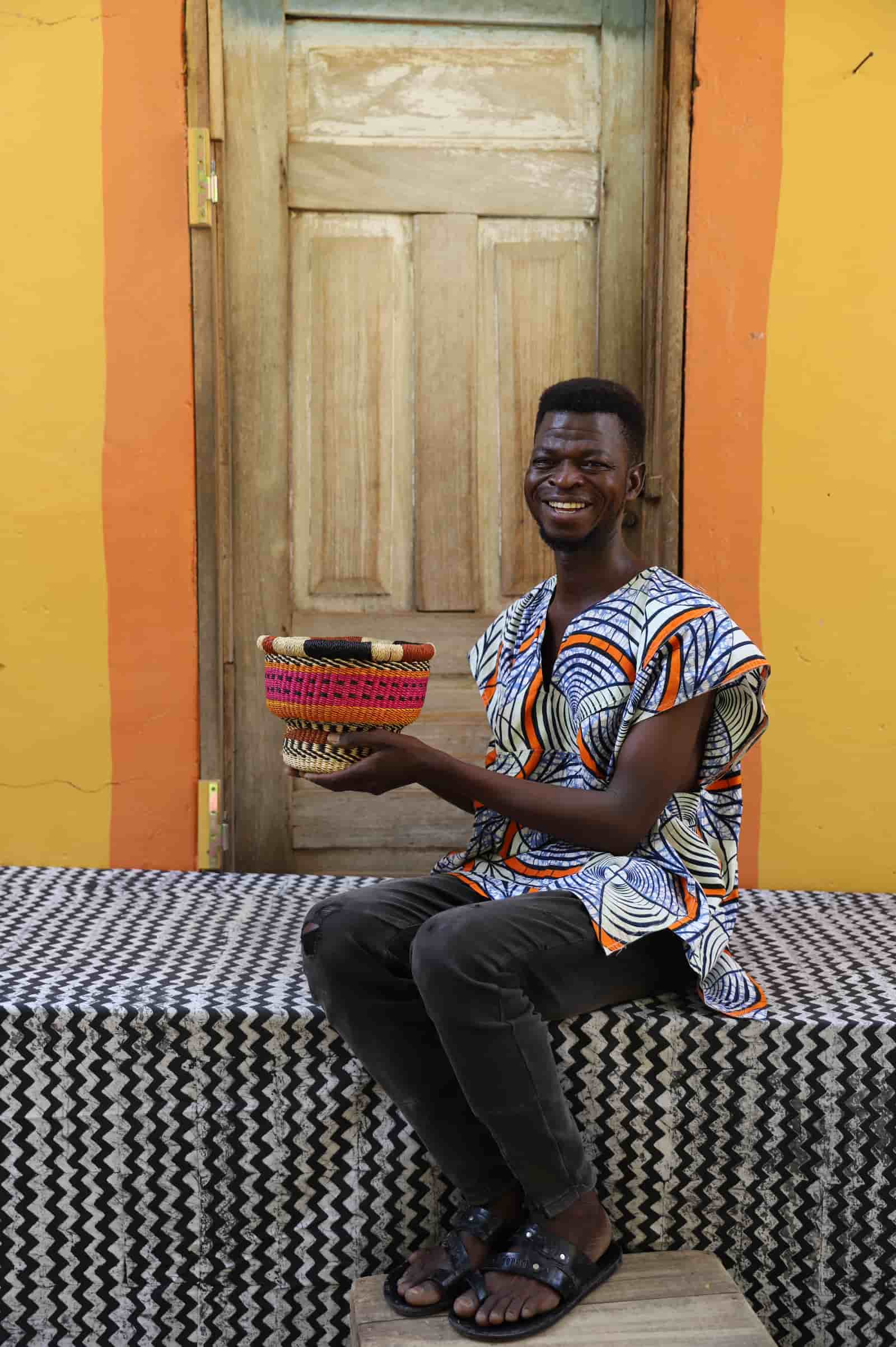 Man holding a woven basket in front of a colorful wall with a wooden door.