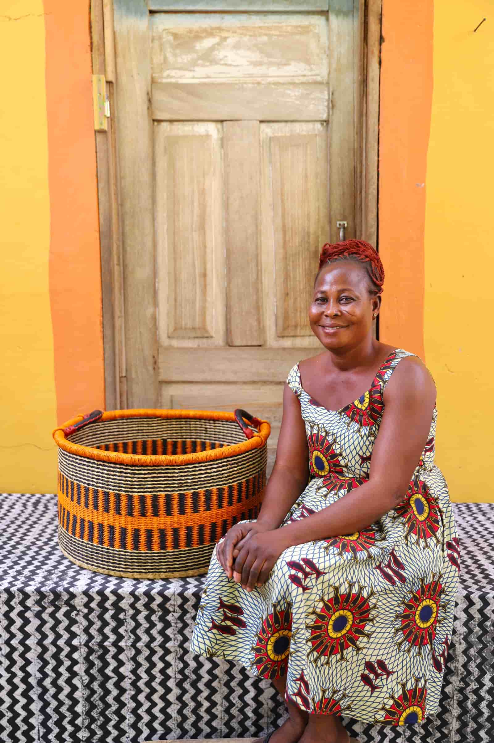 Woven Tub (Large) with woman weaver handwoven in Ghana sitting on black and white cloth and wooden door in background
