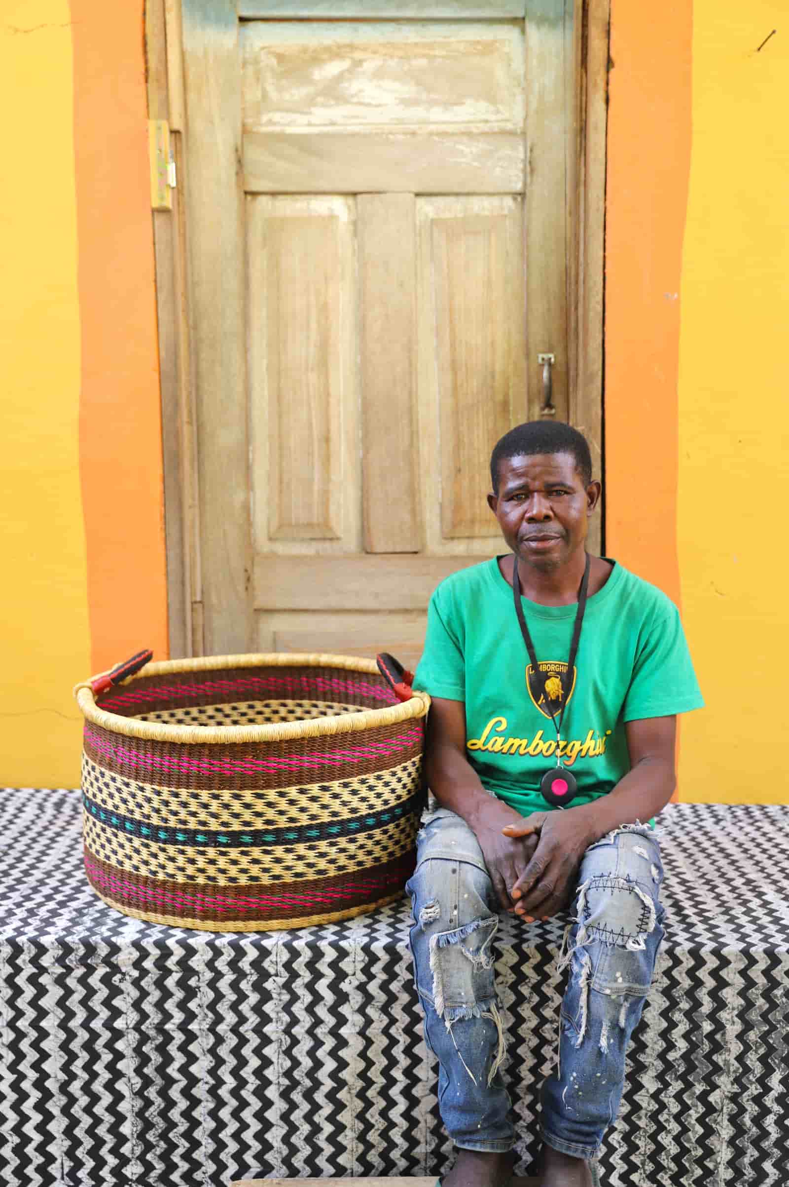 Woven Tub (Large) with man weaver handwoven in Ghana sitting on black and white cloth and wooden door in background

