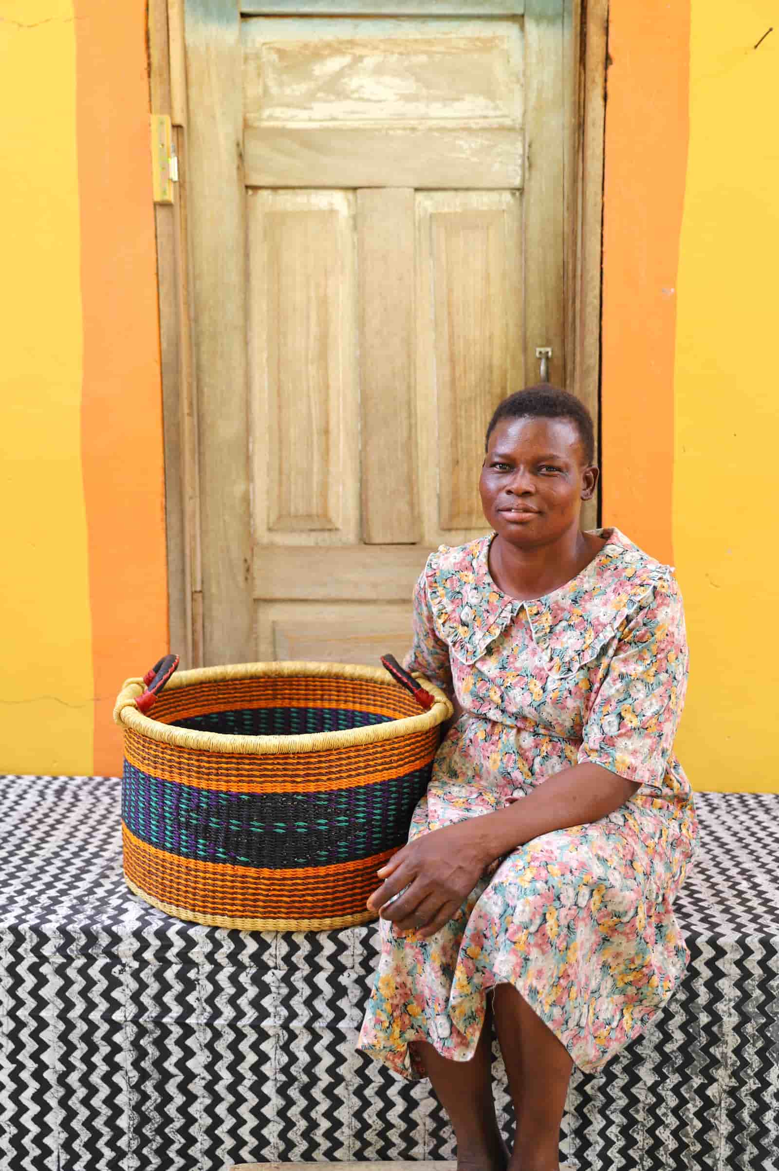 Woven Tub (Medium) with woman weaver handwoven in Ghana sitting on black and white cloth and wooden door in background