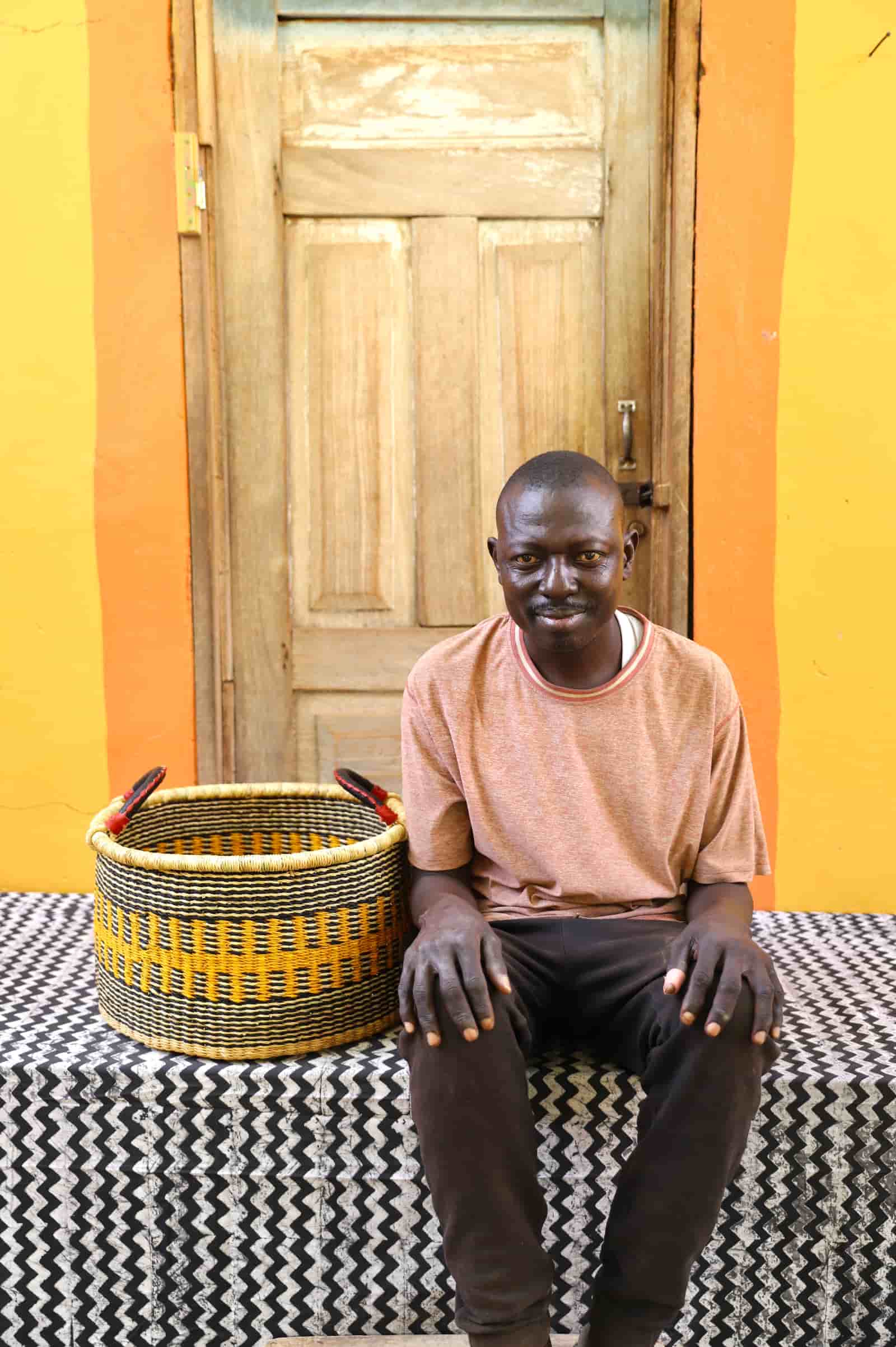 Woven Tub (Small) with man weaver handwoven in Ghana sitting on black and white cloth and wooden door in background