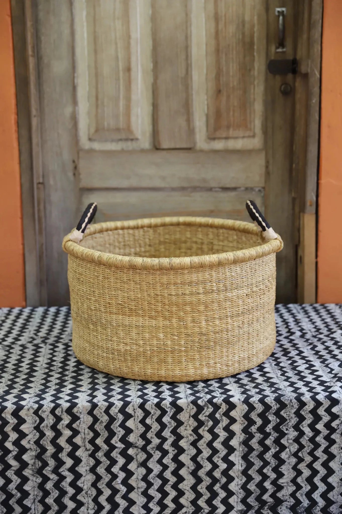 Woven Tub (Medium) handwoven in Ghana sitting on black and white cloth with wooden door background
