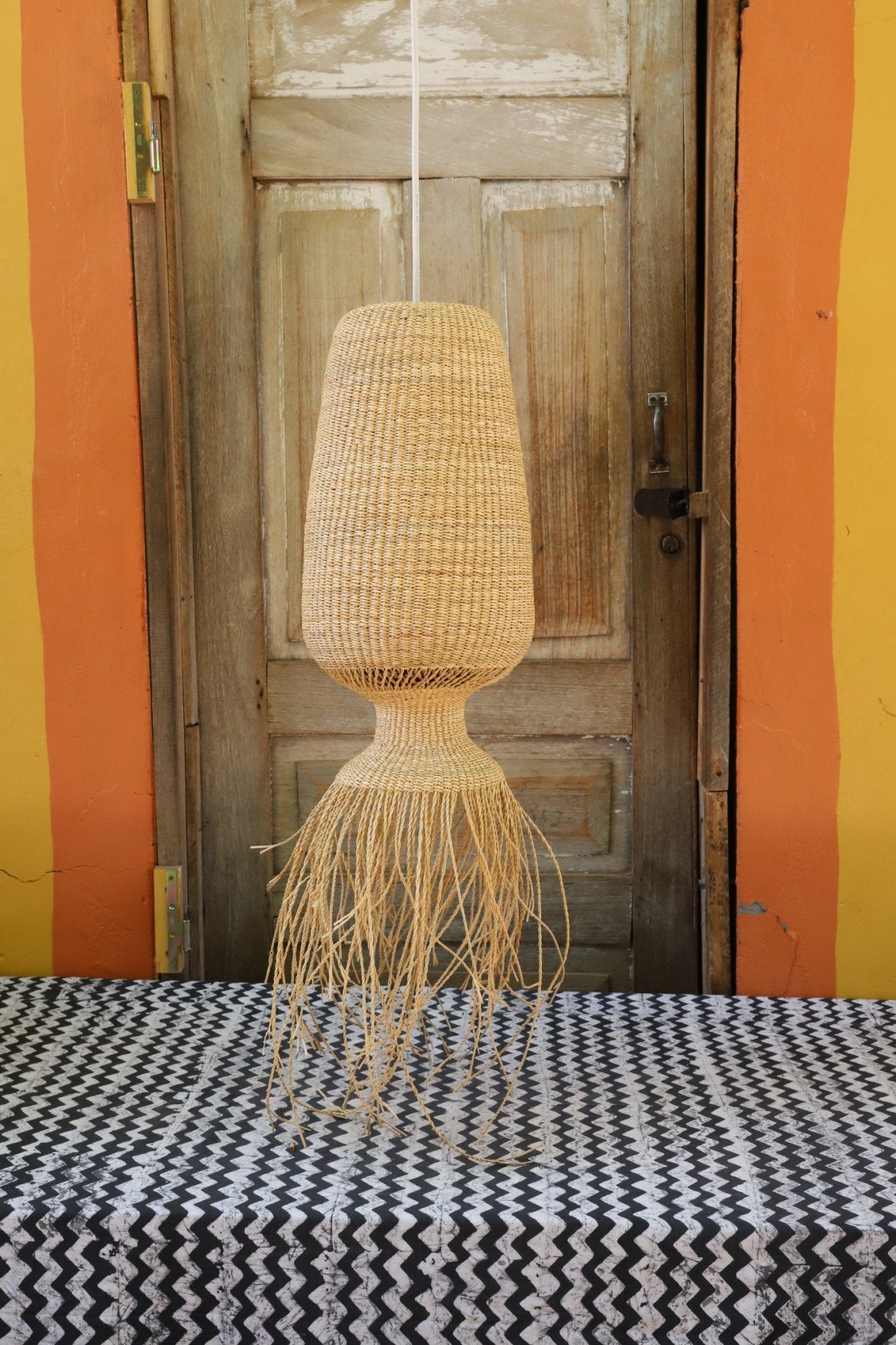 Woven lamp against a wooden wall with colorful striped background