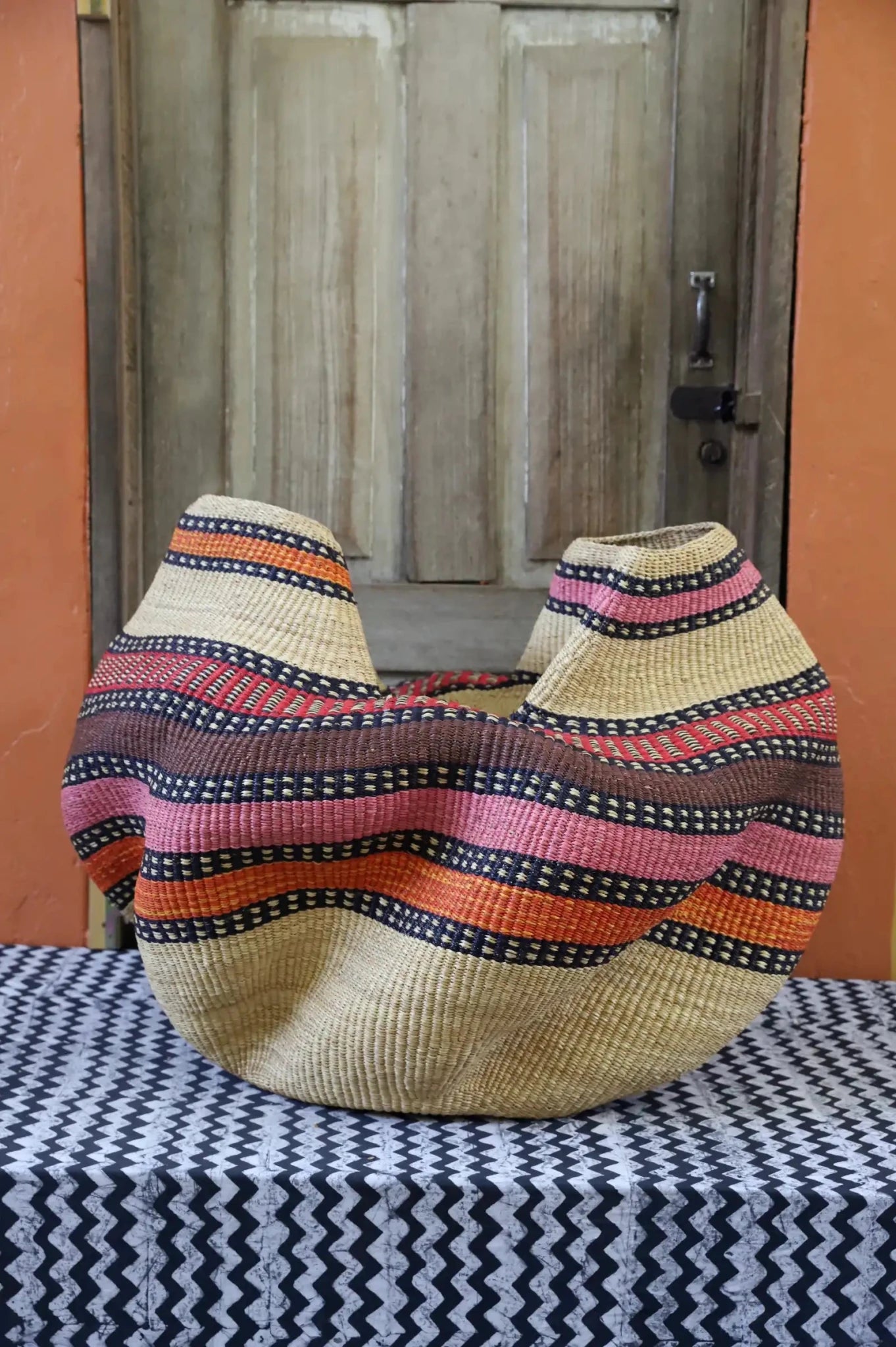 A colorful, handwoven piece sitting on a black and white cloth against a wooden door