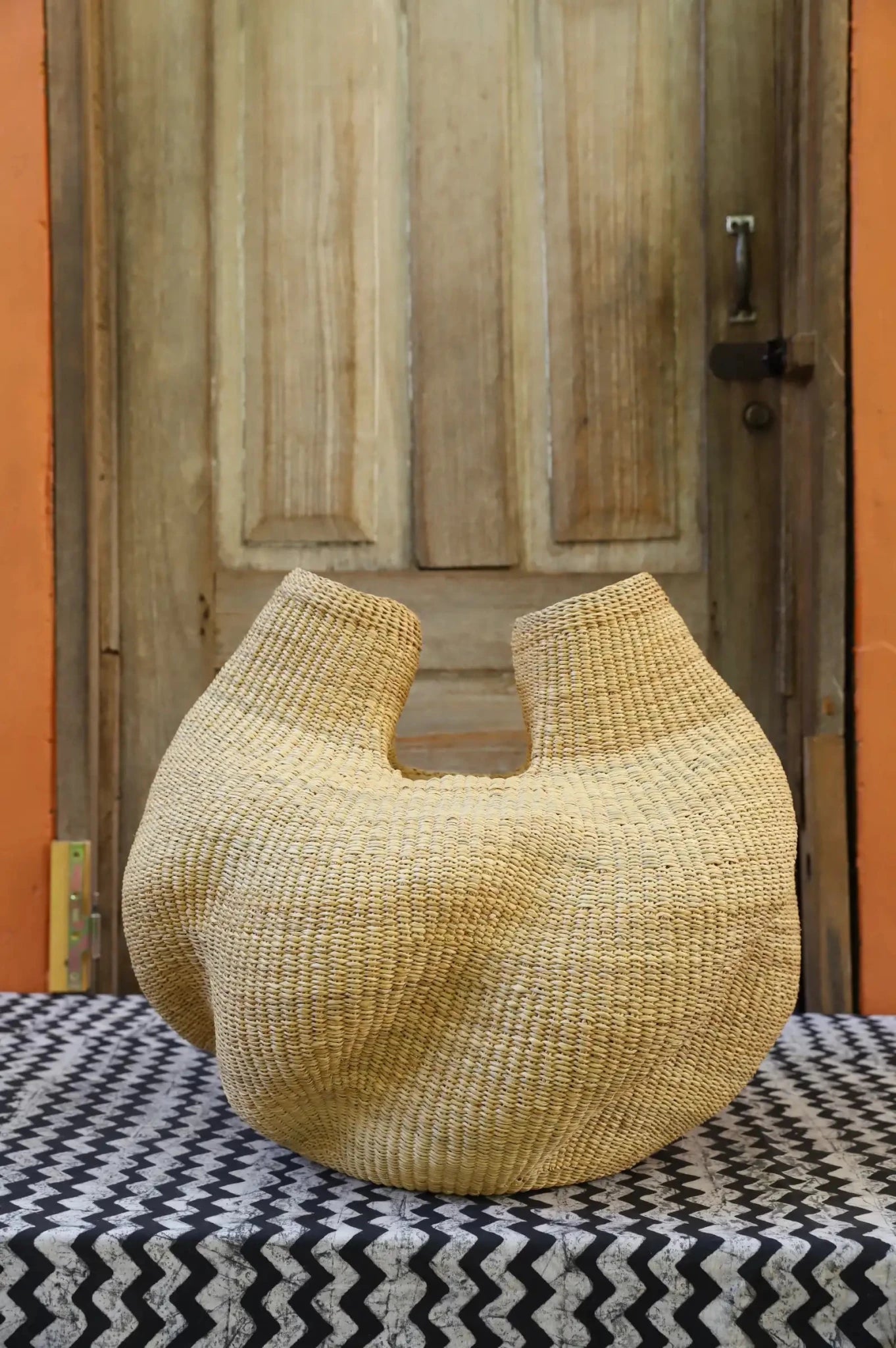 A handwoven piece sitting on a black and white cloth against a wooden door