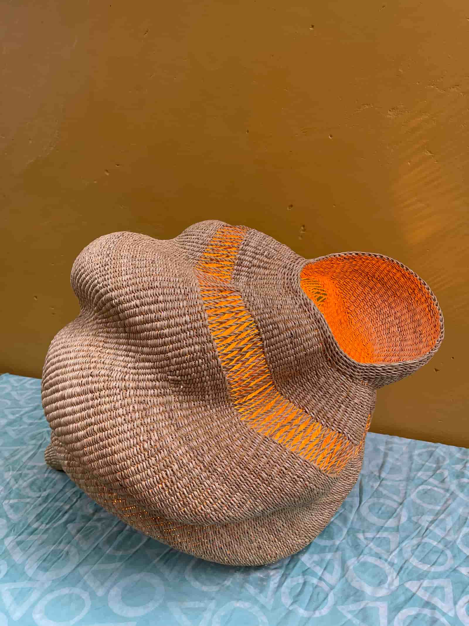 Woven conch-shaped lampshade on a patterned cloth.