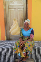 Woman sitting on a bench in front of a colorful wall with a woven lamp hanging.
