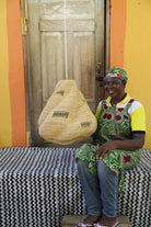 Woman sitting on a bench holding a woven basket against a colorful wall.