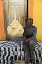 Woman sitting on a bed with a woven basket in front of a wooden door.