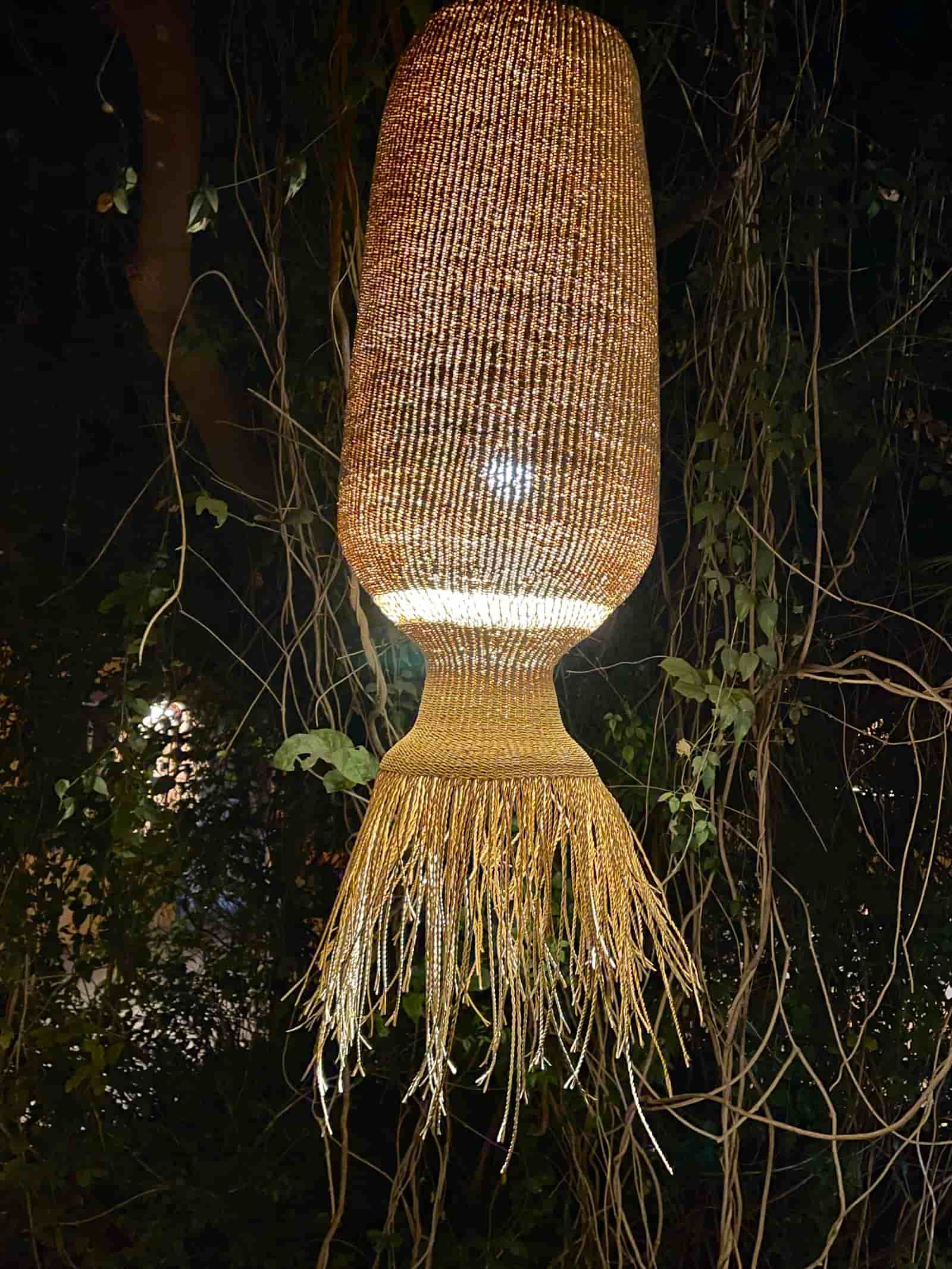 Woven outdoor lamp with fringe detail against a dark background