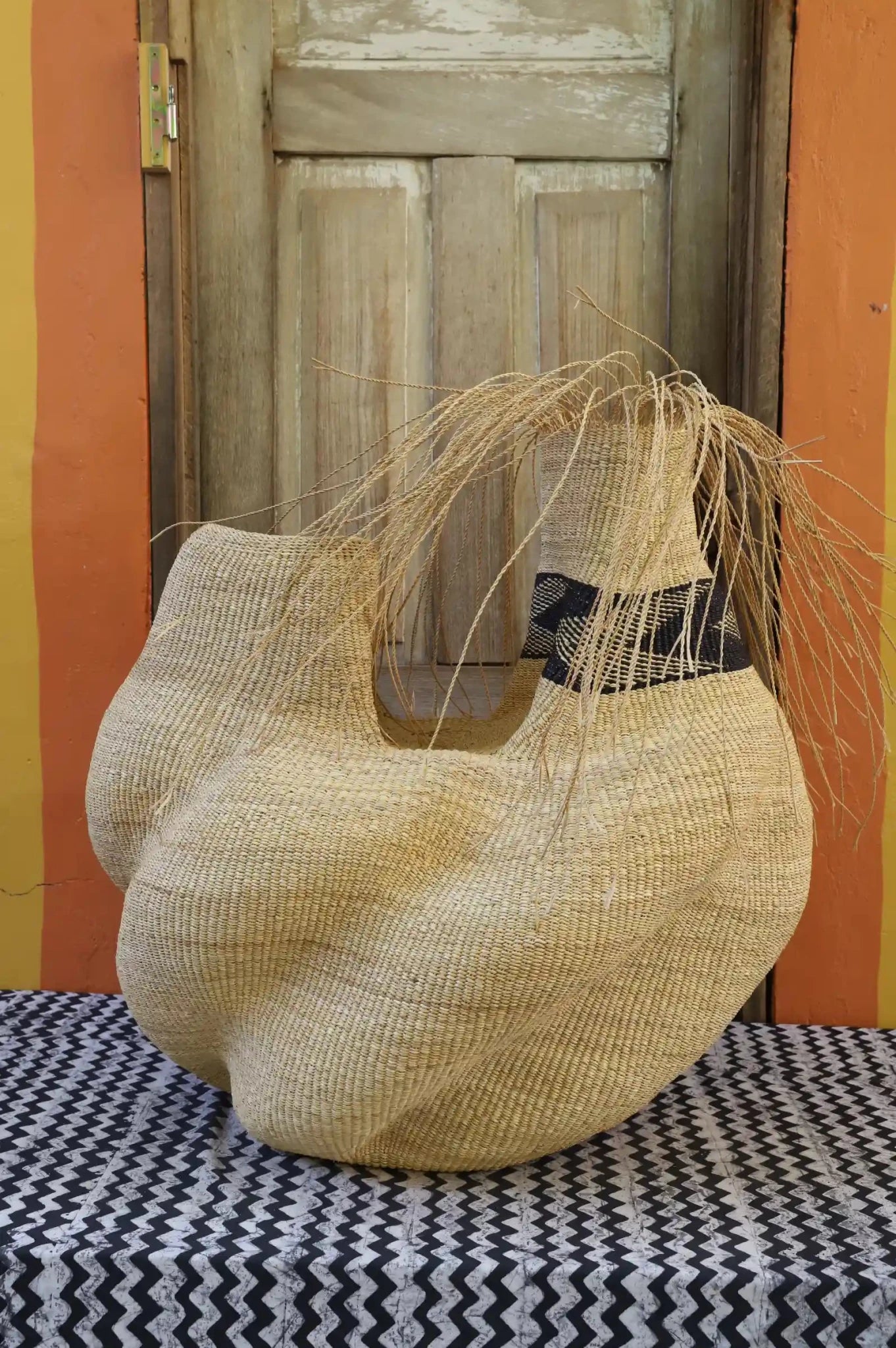 A handwoven piece sitting on a black and white cloth with decorative straw branching out against a wooden door.