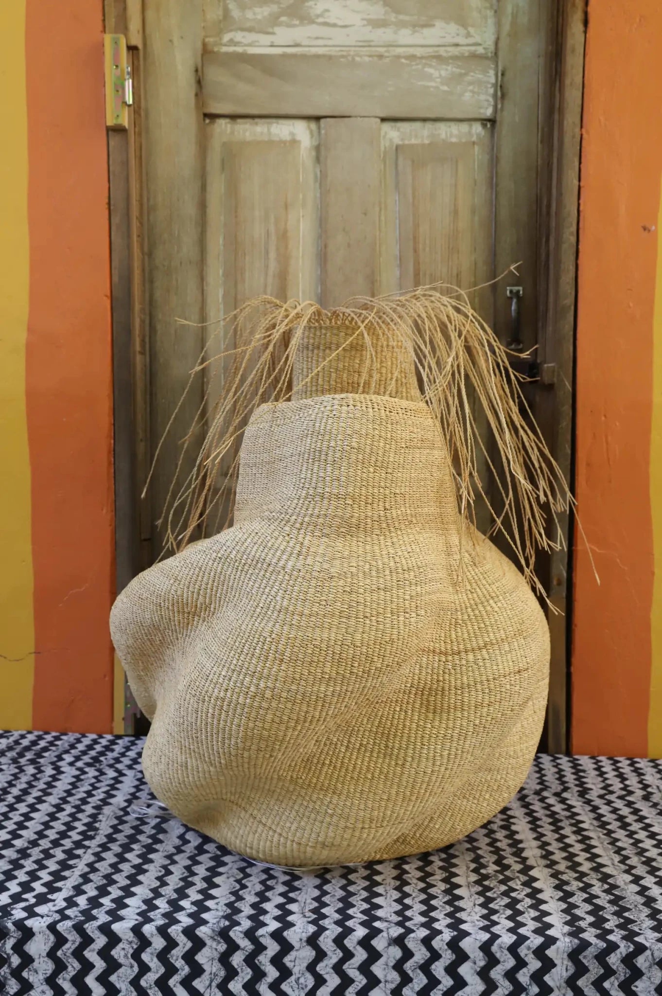 Decorative basket with stylish straw branching out on a black and white cloth against a wooden door.