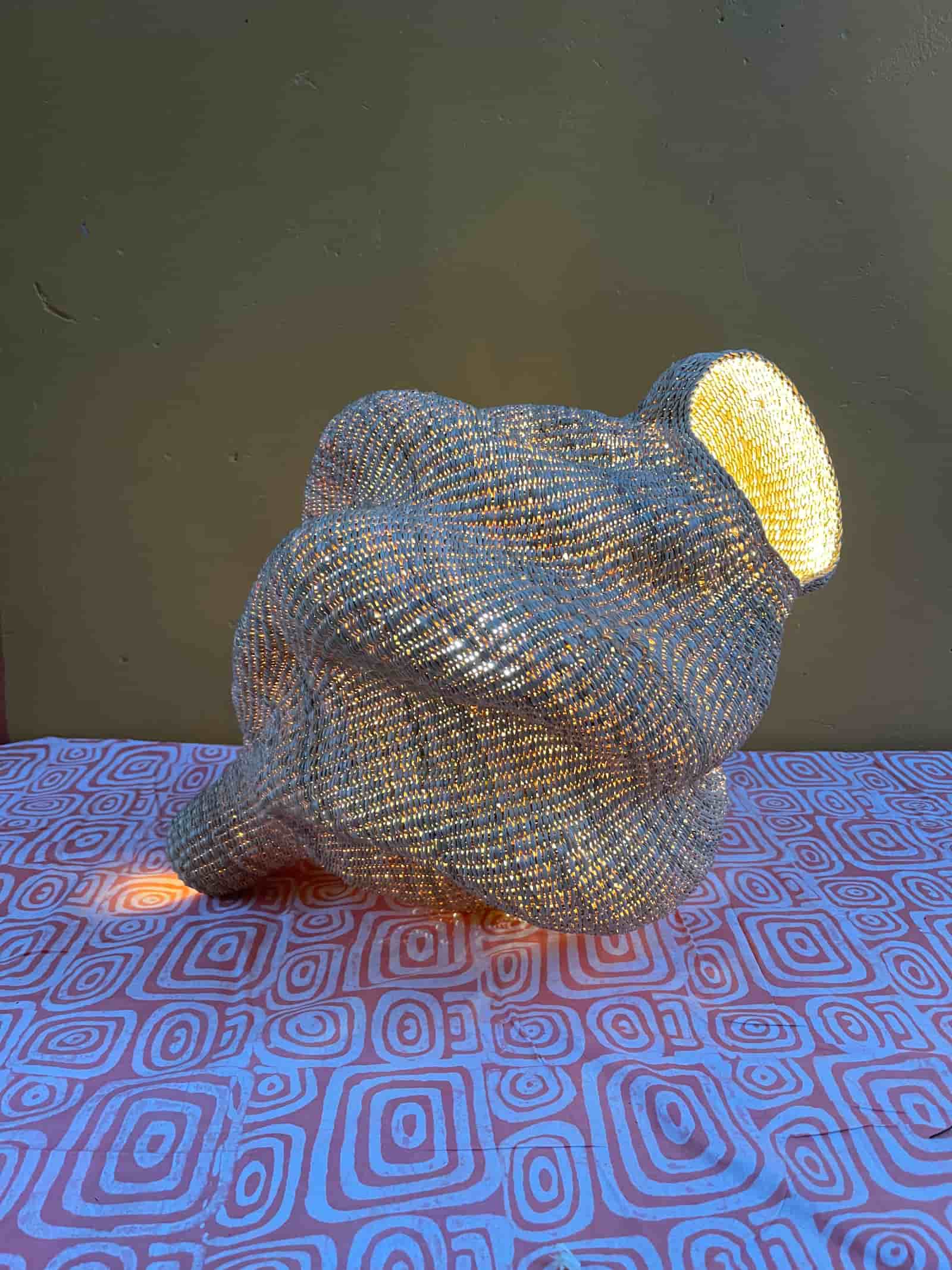 Woven conch-shaped lampshade on a black and white patterned cloth with a wooden door in the background.