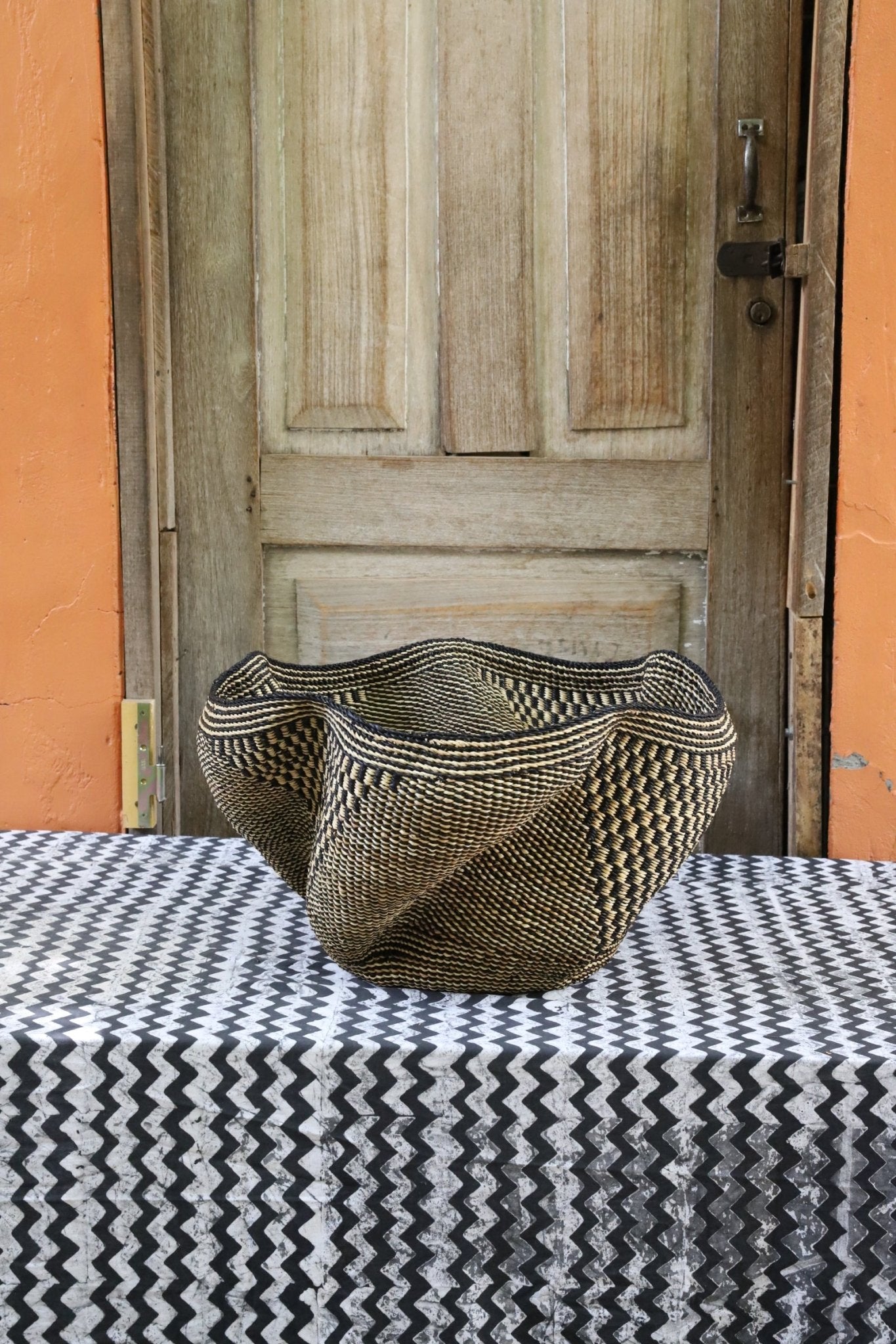 Decorative handwoven straw basket with colorful patterns on a black and white cloth against a wooden door.