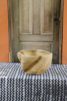 Decorative handwoven straw basket with colorful patterns on a black and white cloth against a wooden door.