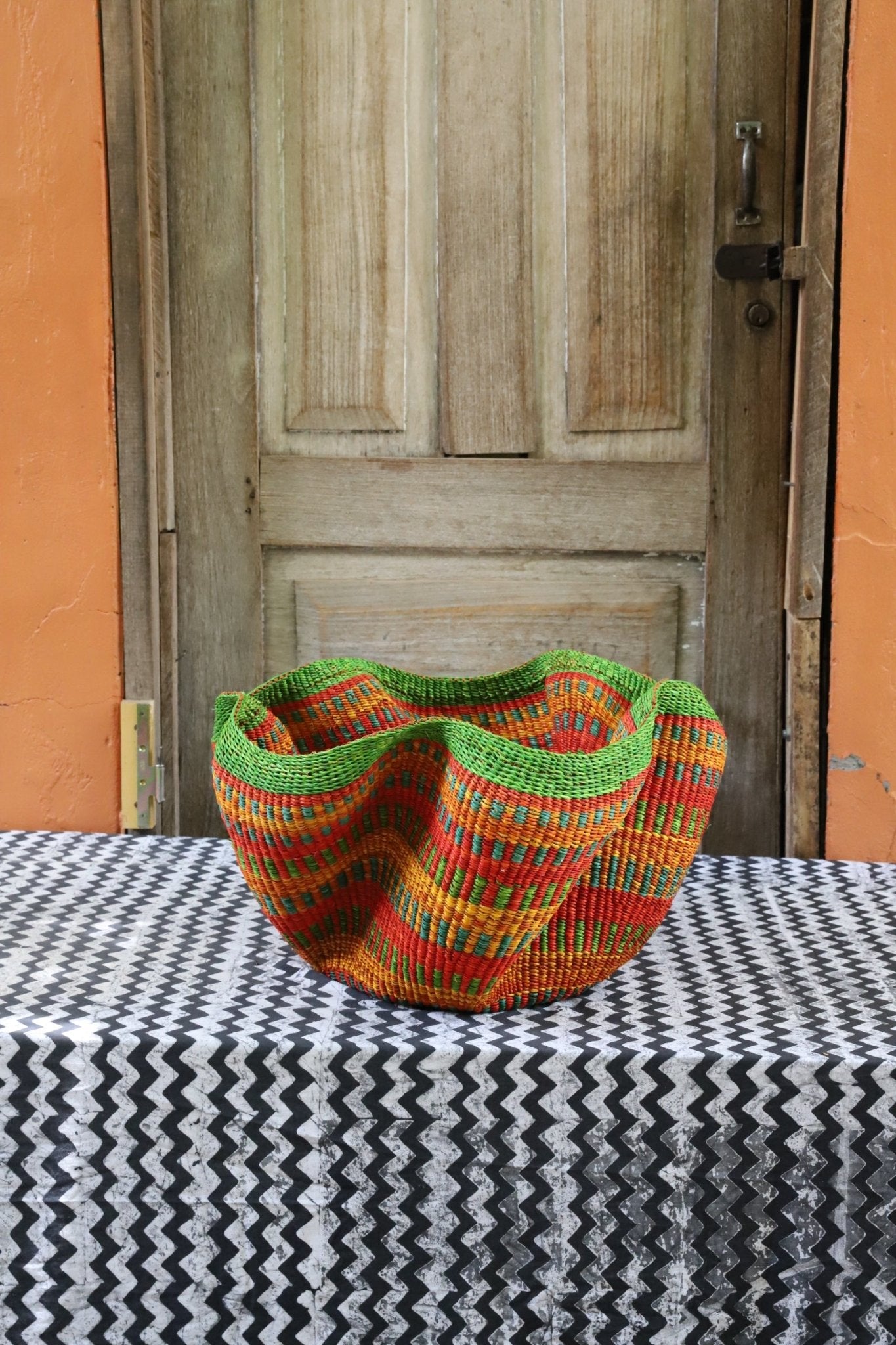 Decorative handwoven straw basket with colorful patterns on a black and white cloth against a wooden door.