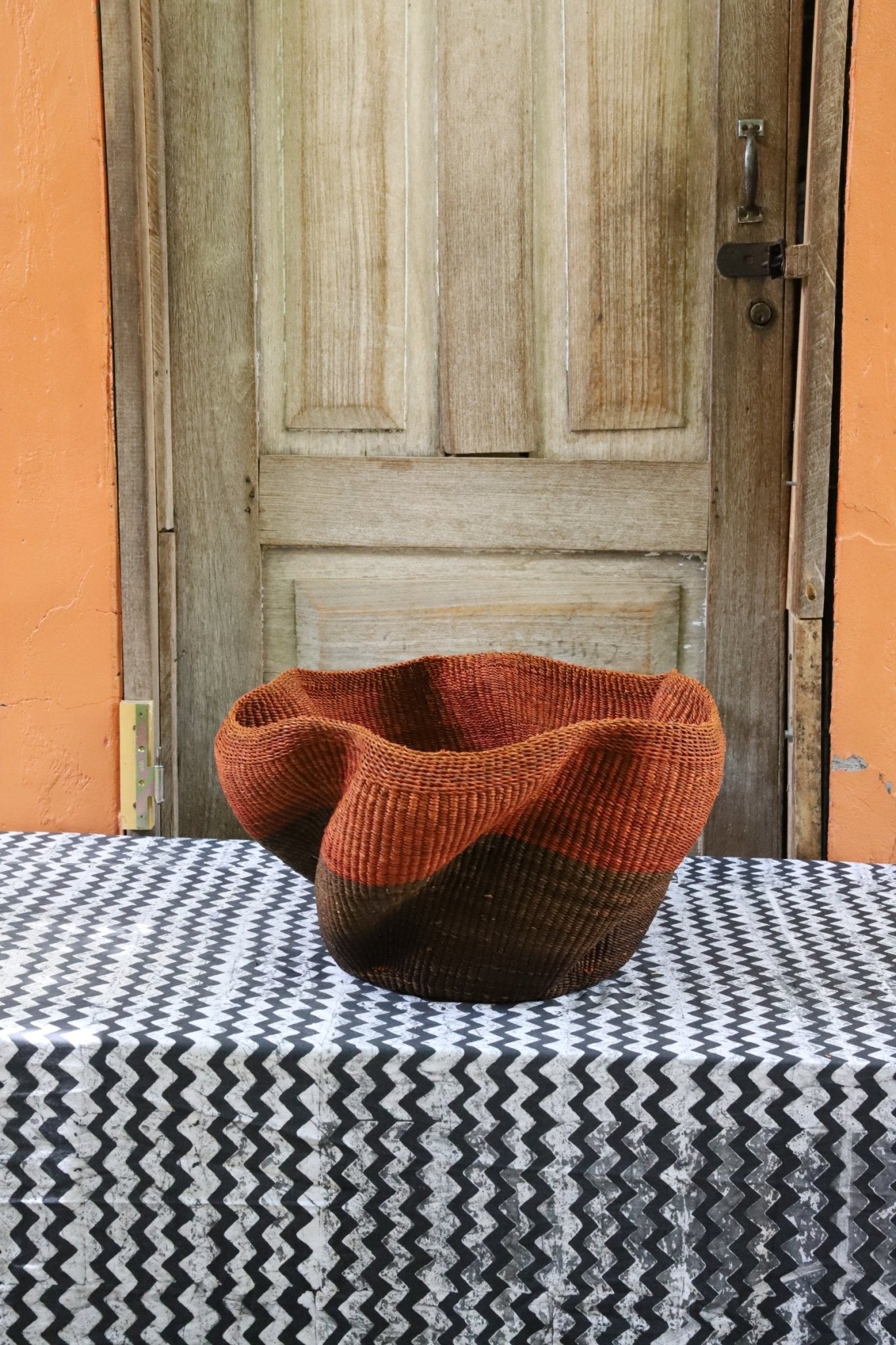 Decorative handwoven straw basket with colorful patterns on a black and white cloth against a wooden door.