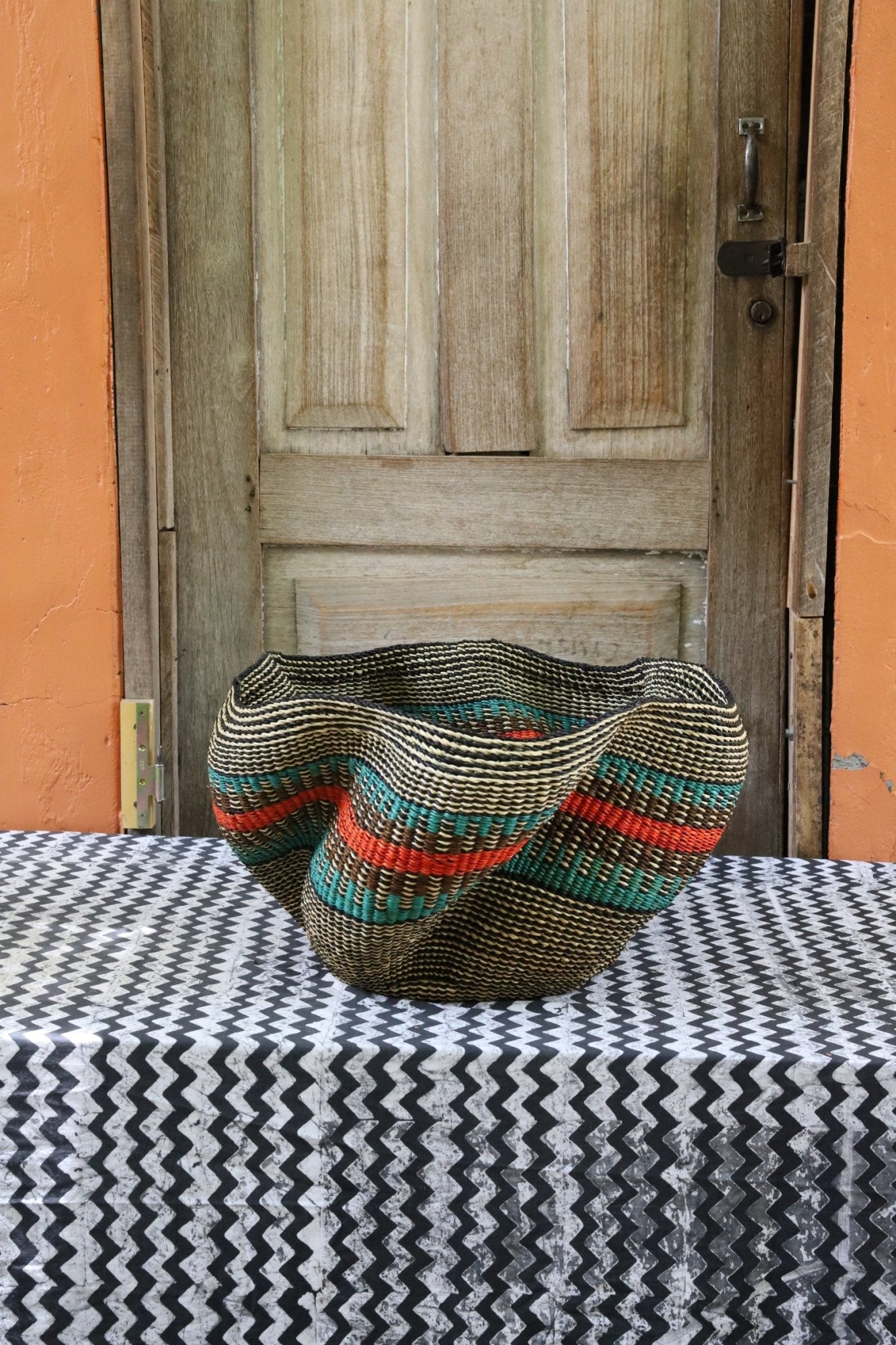 Decorative handwoven straw basket with colorful patterns on a black and white cloth against a wooden door.