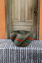 Decorative handwoven straw basket with colorful patterns on a black and white cloth against a wooden door.