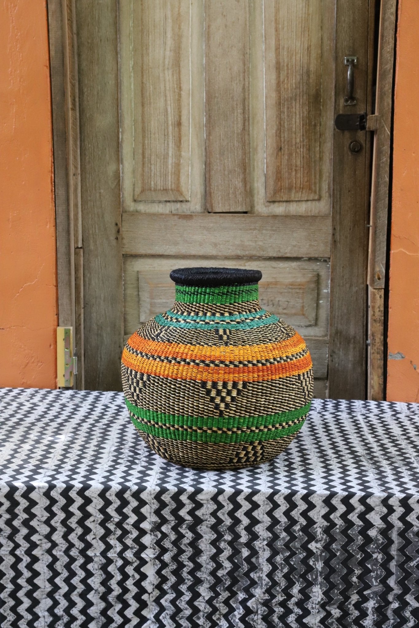 Decorative handwoven basket with colorful patterns on a black and white cloth against a wooden door.