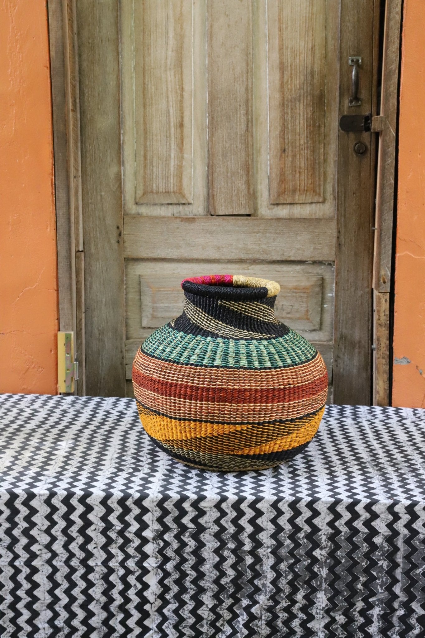 Decorative handwoven basket with colorful patterns on a black and white cloth against a wooden door.