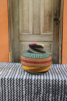Decorative handwoven basket with colorful patterns on a black and white cloth against a wooden door.