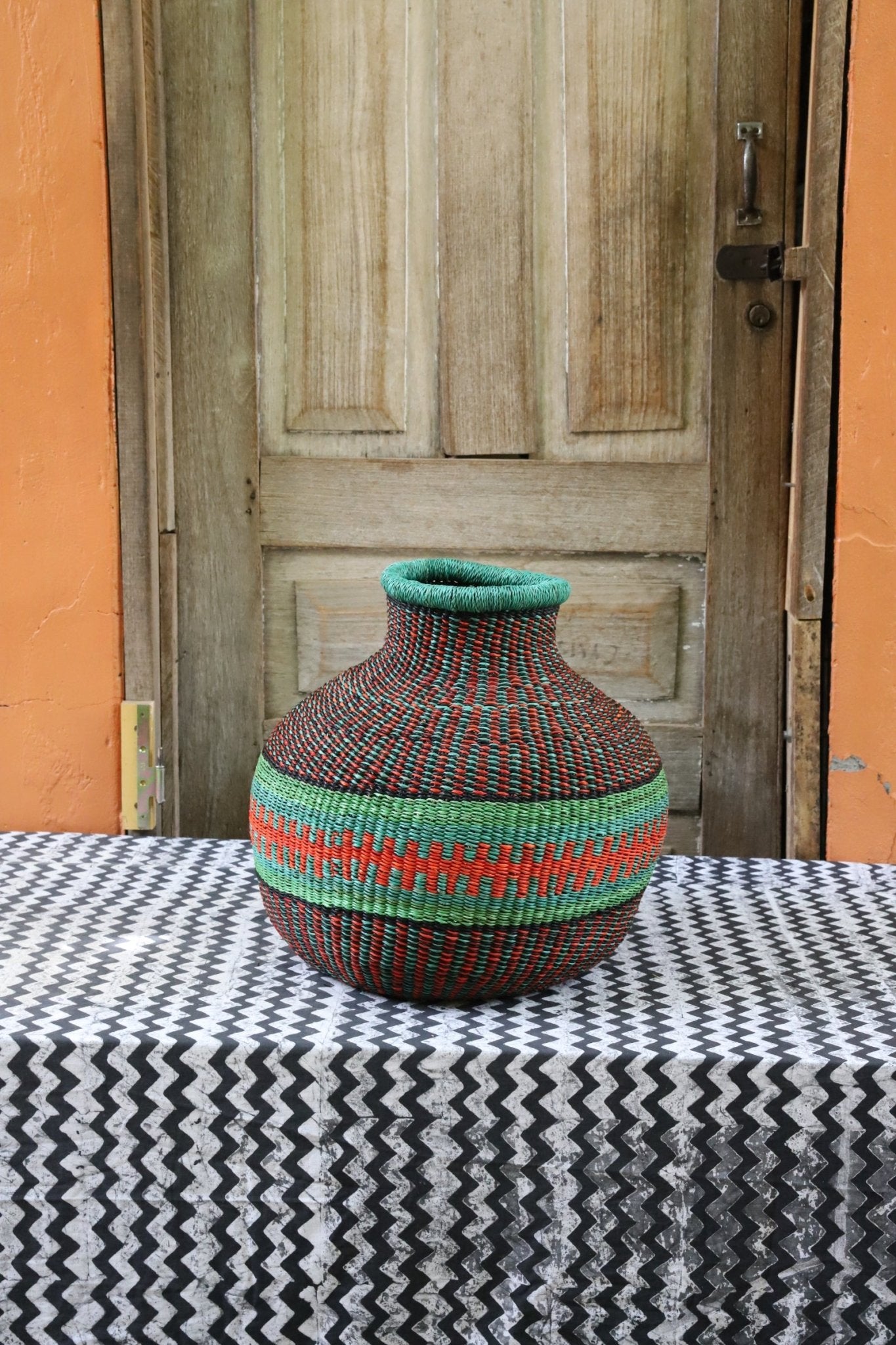 Decorative handwoven basket with colorful patterns on a black and white cloth against a wooden door.