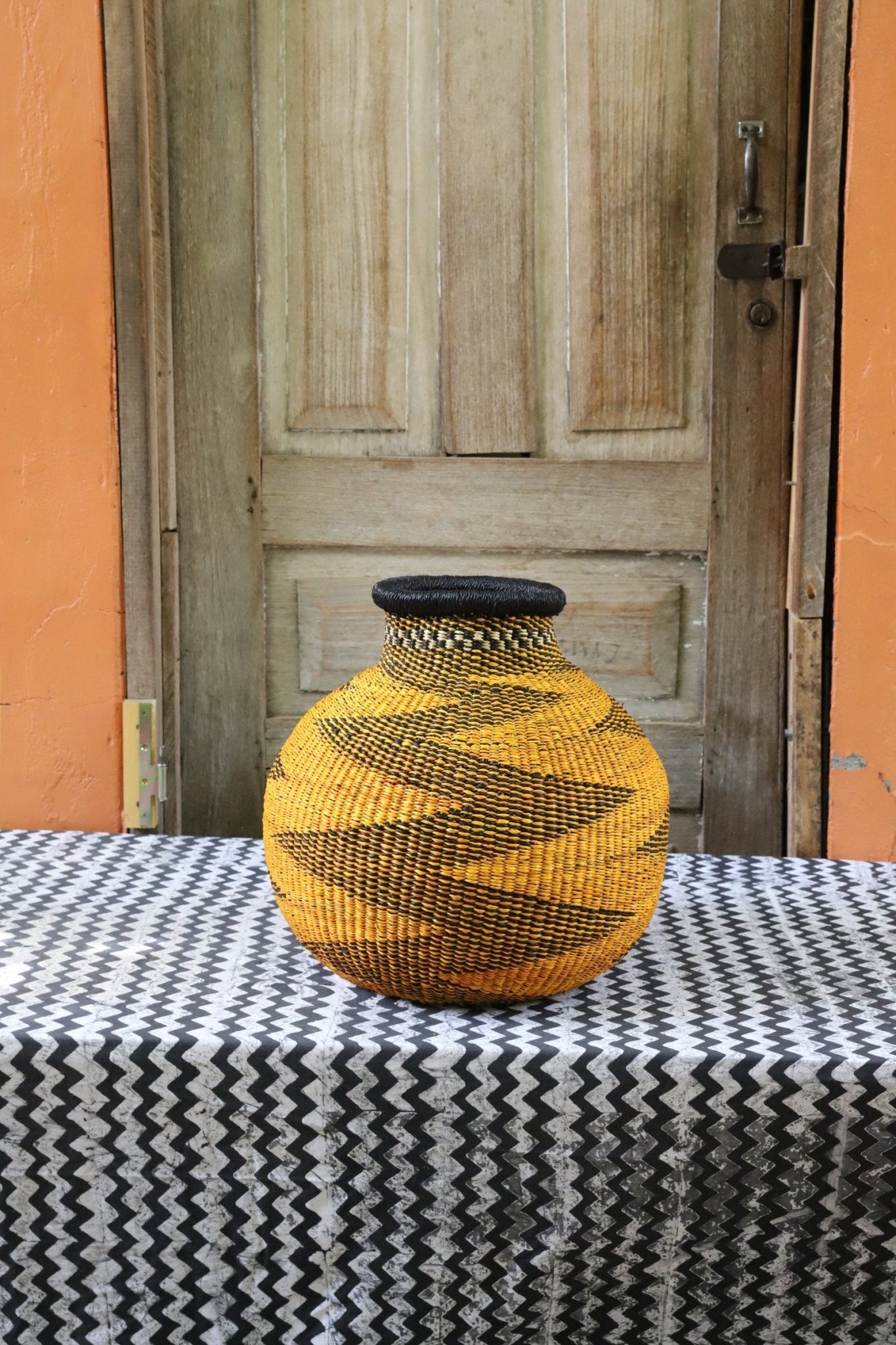 Decorative handwoven basket with colorful patterns on a black and white cloth against a wooden door.