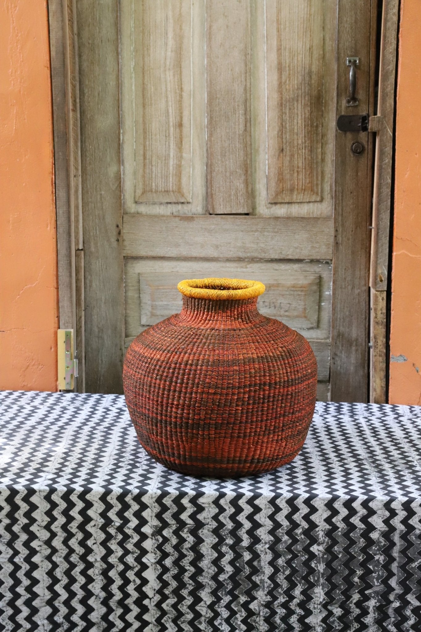 Decorative handwoven basket with colorful patterns on a black and white cloth against a wooden door.
