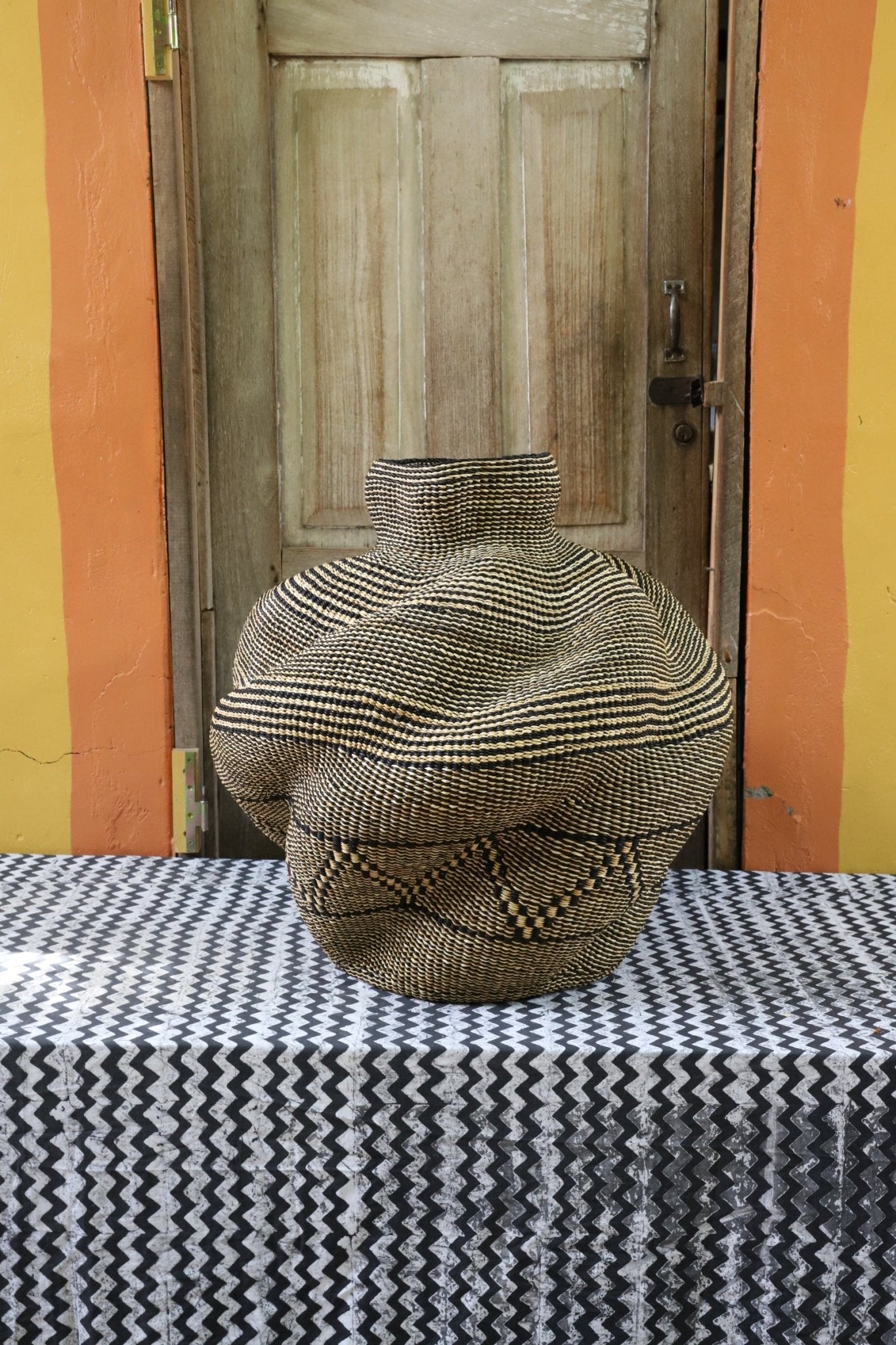 A handwoven piece with decorative curves sitting on a black and white cloth against a wooden door