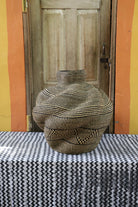 A handwoven piece with decorative curves sitting on a black and white cloth against a wooden door