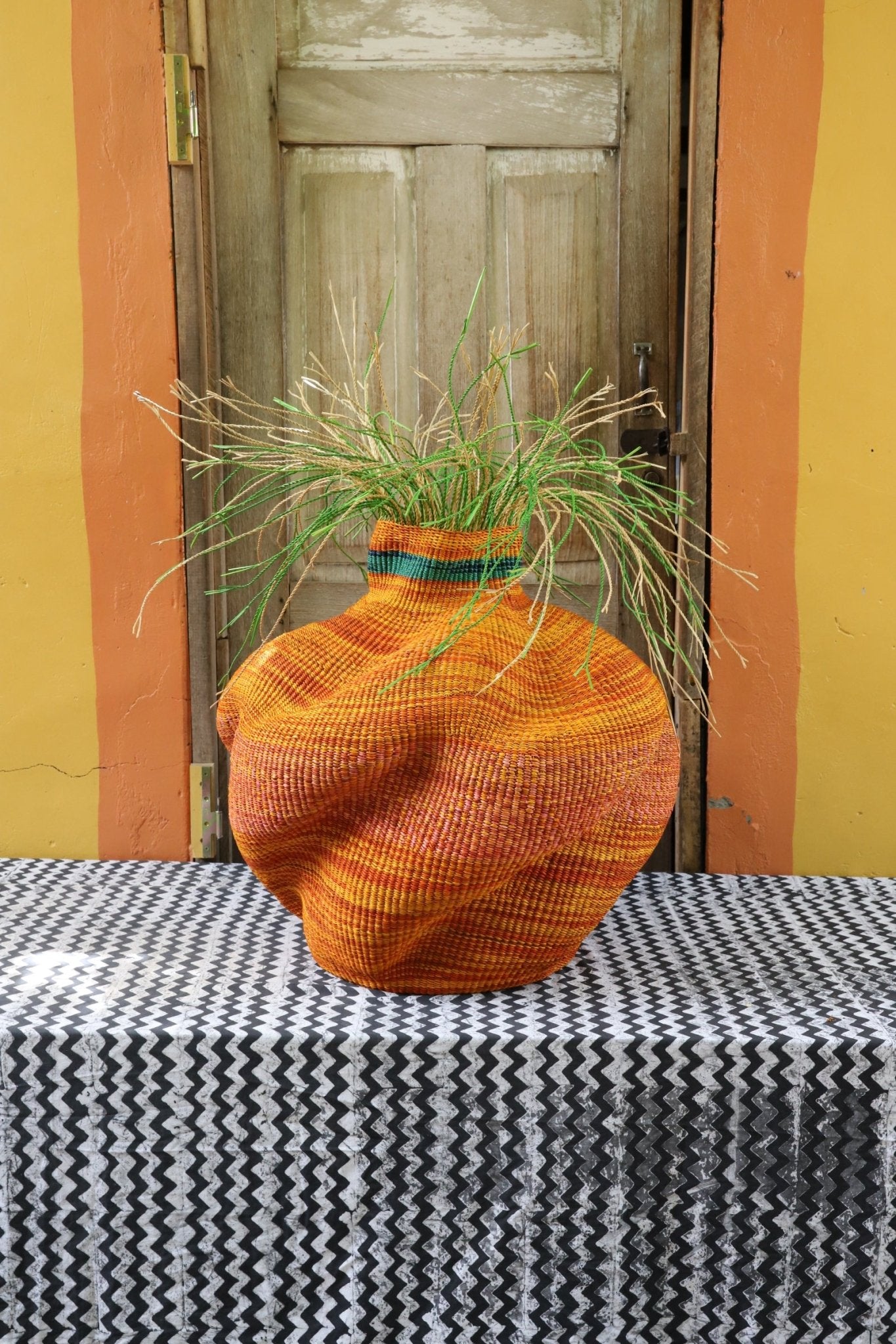 A colorful, handwoven piece sitting on a black and white cloth with decorative straw branching out. 