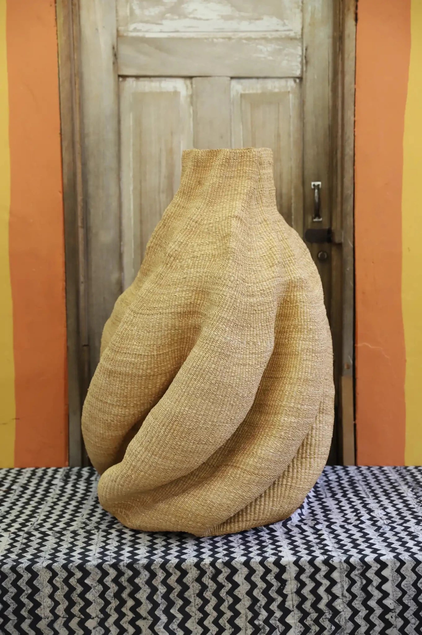 A handwoven piece with decorative curves sitting on a black and white cloth against a wooden door