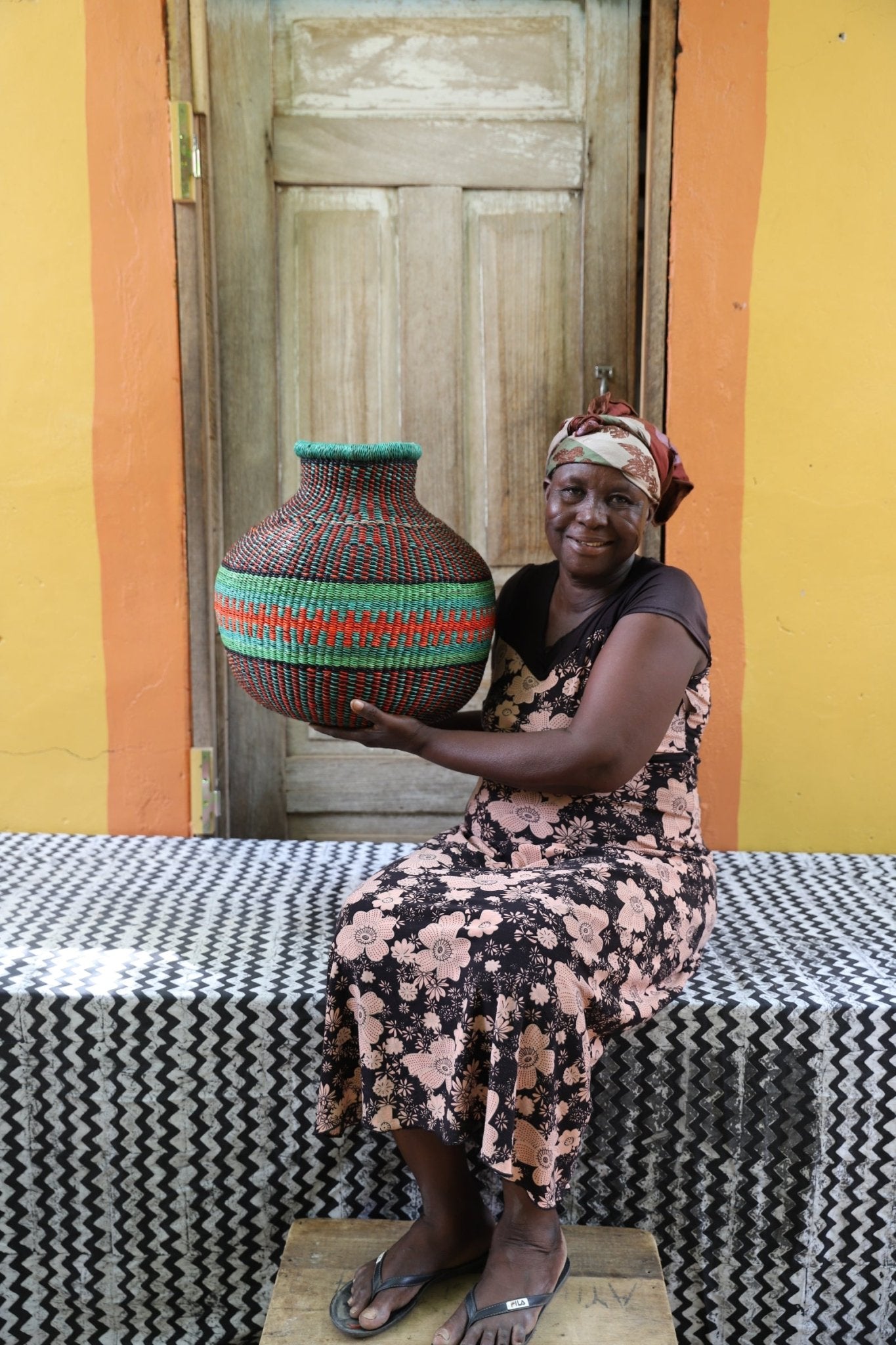 Artisan holding a colorful woven storage basket  on a black and white cloth against a wooden door.