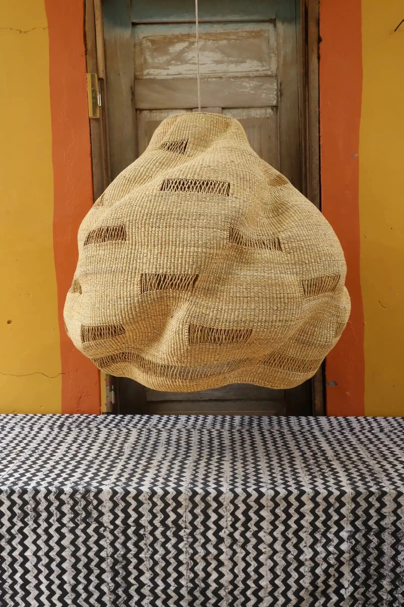 Woven basket hanging on a door with a patterned tablecloth.