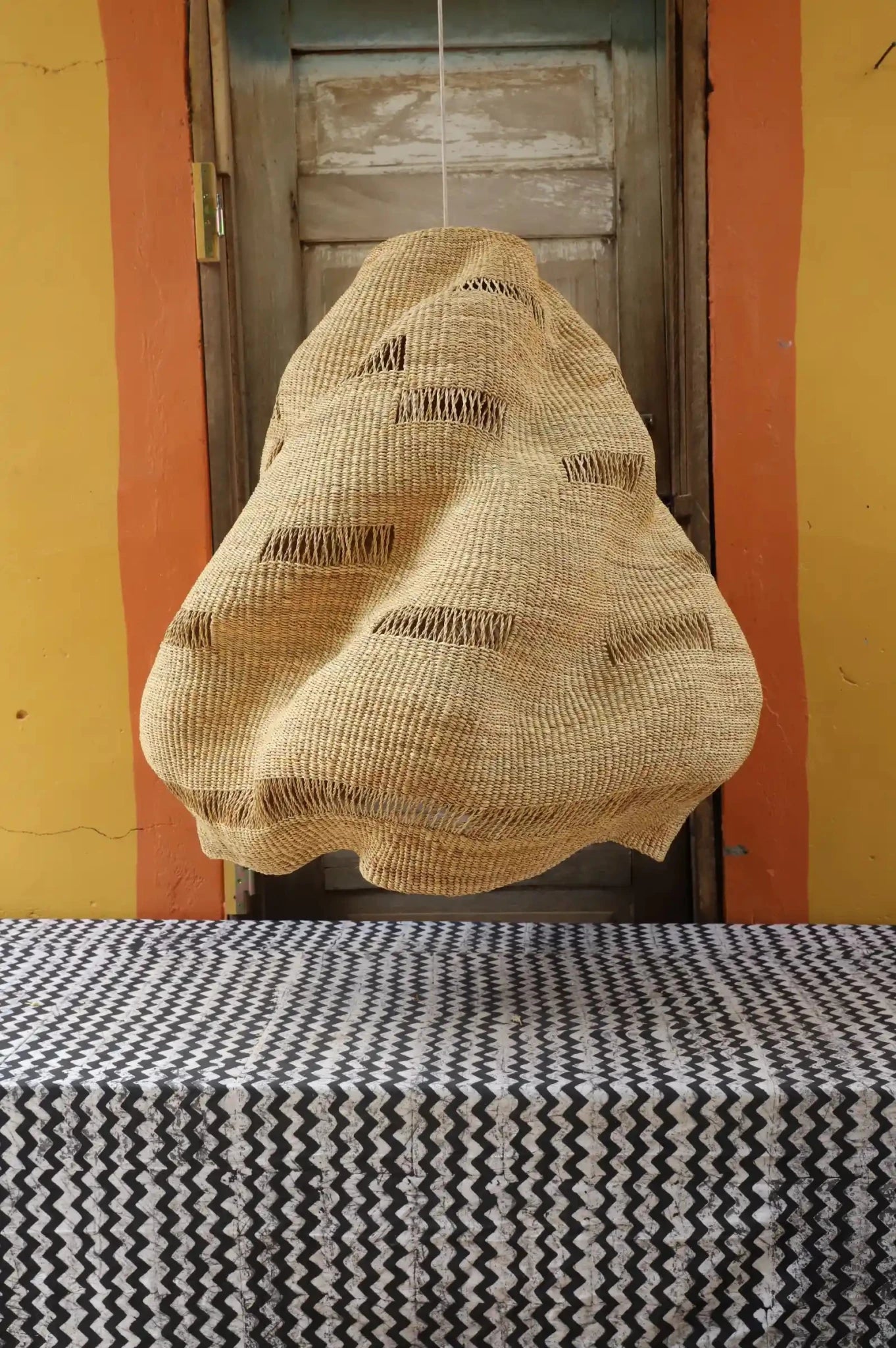 Large woven basket  sculpture on a table with a yellow wall and wooden door in the background