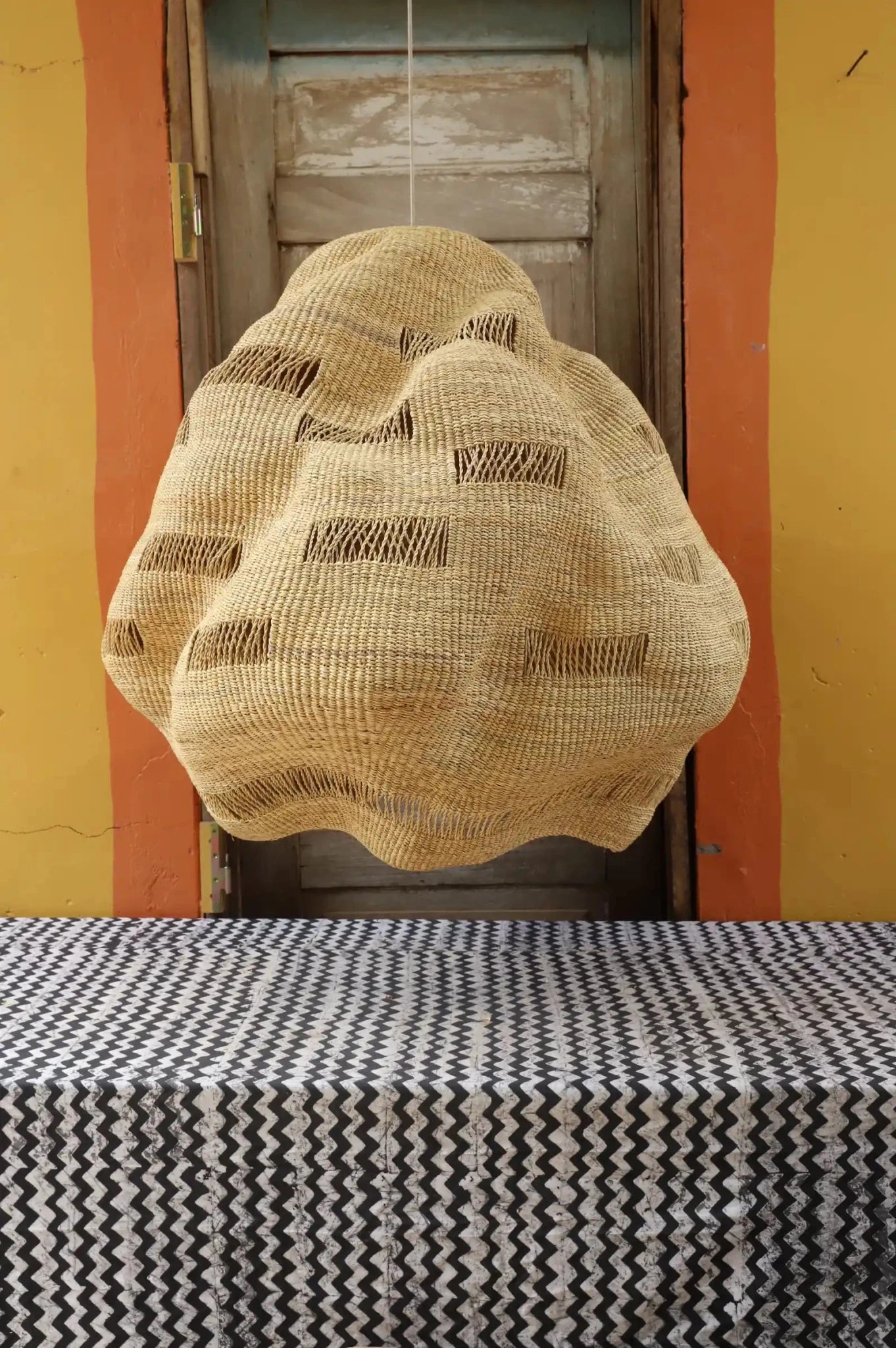 Woven basket hanging on a door with a patterned tablecloth in the foreground