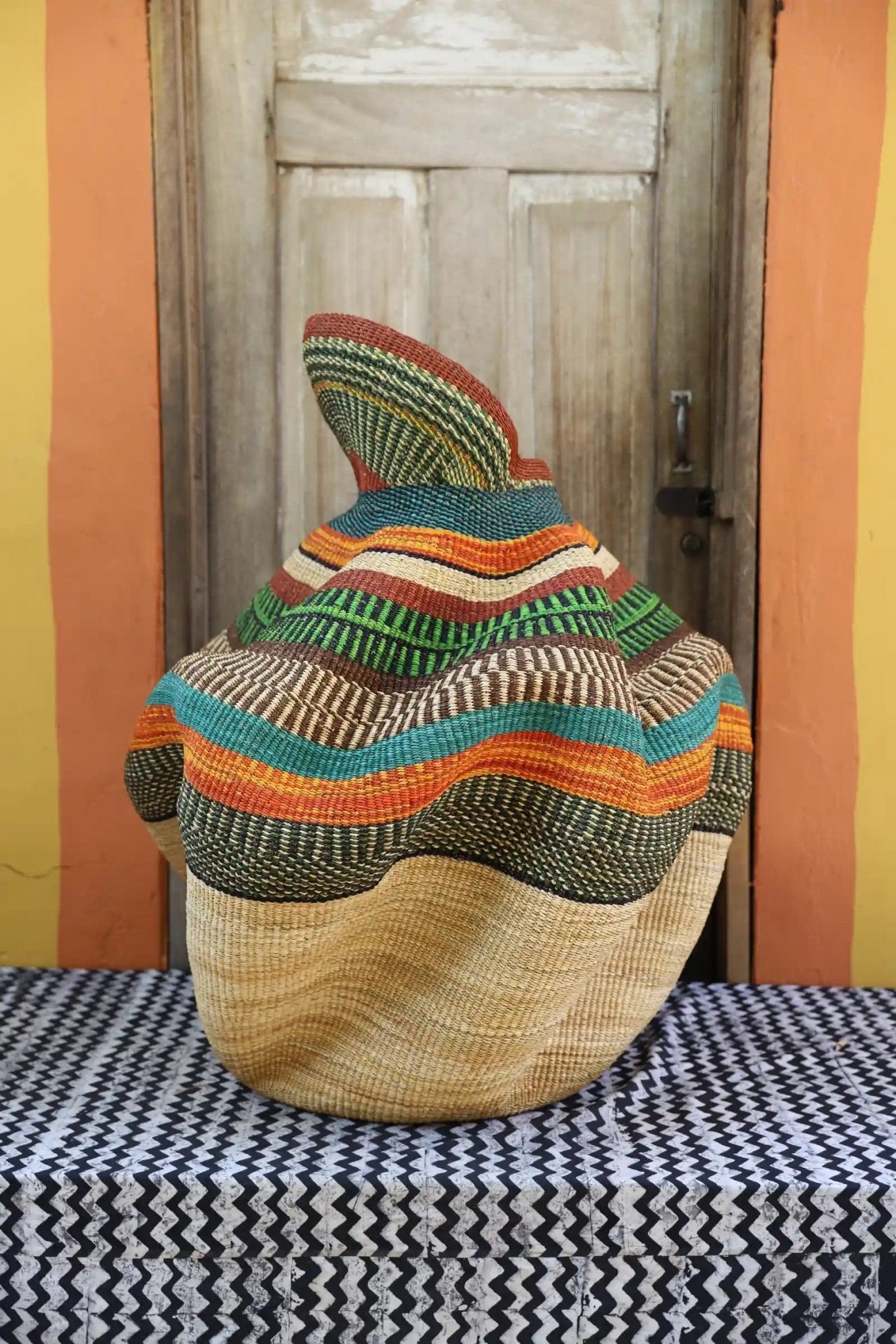 A colorful, handwoven piece with decorative curves sitting on a black and white cloth against a wooden door